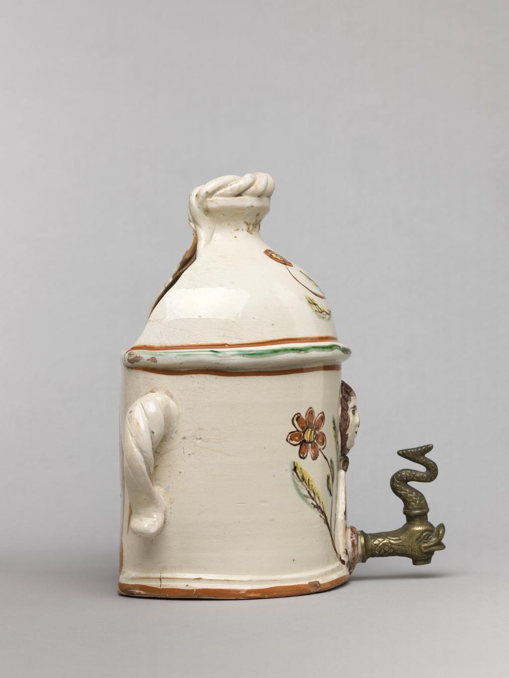 An image of Wall cistern. Lötscher, Andreas (Swiss). Production Place: Switzerland, Canton Graubünden, Sant Antönien. The cistern is semi-circular in plan with straight sides and two twisted handles on opposing sides. The domed top is cut away at the back, and is surmounted by an applied twist. In the middle of the front, a mask in relief is flanked by painted sprays of flowers, and below it, there is a hole in which is inserted a brass tap in the from of a monster's head. Buff earthenware, coated overall except for the back with white slip, and painted in olive-green, red, yellow, and manganese-purple under a clear lead-glaze. Height, whole, 21.5 cm, circa 1823.