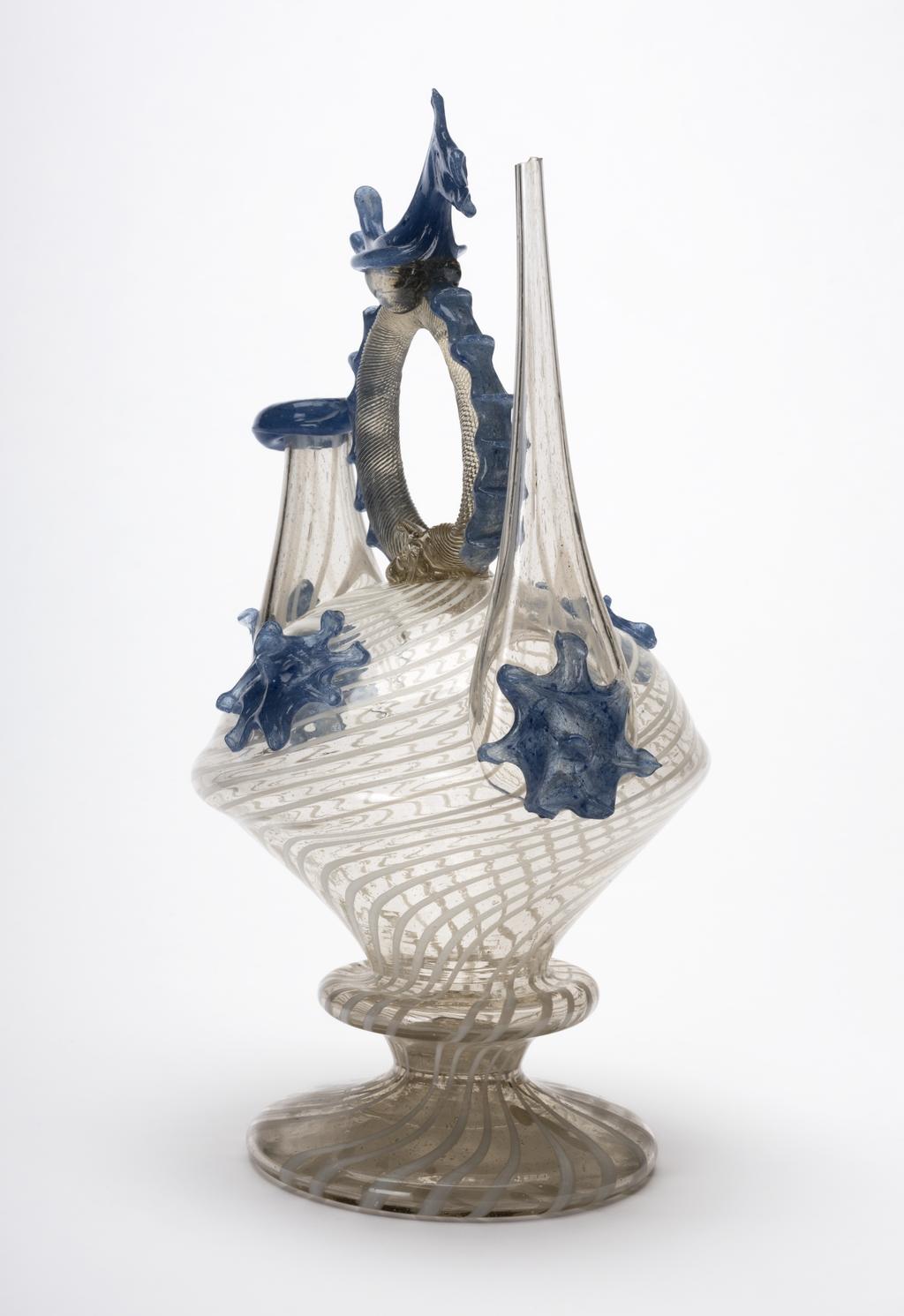 An image of Continental glass. Càntir. Pouring vessel for wine. Unknown glasshouse, Spain, Catalonia. Pale yellowish bubbly glass with opaque white threads, applied blue glass decoration and bird finial. Height, whole, 27.8 cm, width, whole, 17.3 cm, circa 1700-1750, possibly late 17th century. Production Note: A càntir is a vessel for pouring water. The word derives from the Spanish cántaro, a ceramic jug. This form is one of several typical of Catalonian glass production. Sir Ivor and Lady Batchelor Bequest through The Art Fund.
