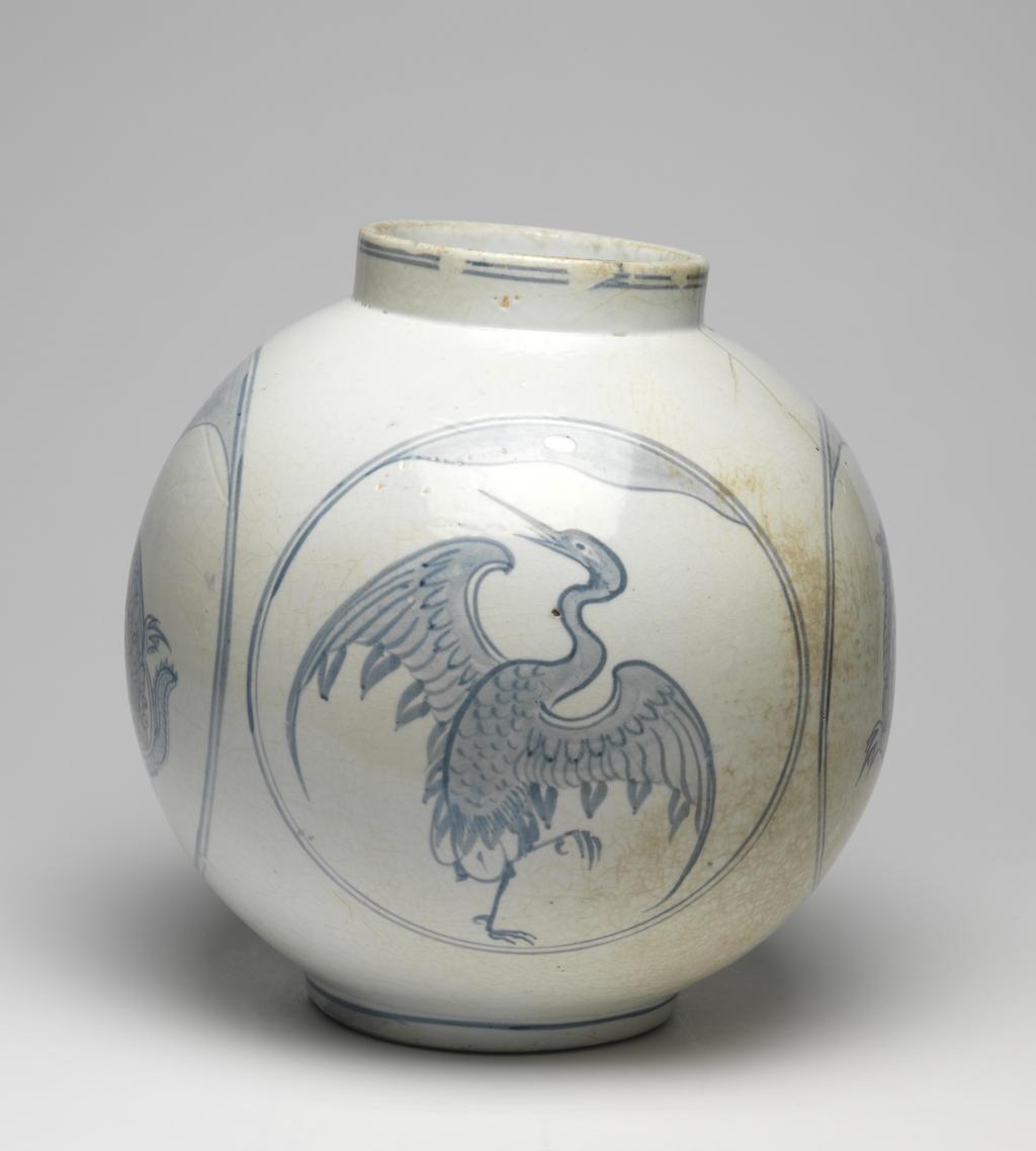 An image of Large jar with tortoise and crane designs. Unknown pottery, Korea, Kwangju, Punwon-ri kilns. The body of this jar is almost globular and the neck straight; the foot is wider than the neck, giving the jar a stable appearance. In four roundels around the sides, divine tortoises and cranes are arranged in alternation, with a cloud or auspicious vapour issuing from the mouth of each tortoise, and with lots of free space around the designs. The glaze is of milky-white colour and crackled, the body is thick and heavy. On the base is an unexplained straight incised line and traces of sandy supports adhere to the footring. Porcelain, thrown, painted in cobalt-blue, and glazed, height, whole, 31.0 cm, diameter, rim, 14.0 cm, diameter, foot, 15.0 cm, circa 1750-1800. Choson Dynasty (1392-1910). Notes: Such jars (hangari) were used as wine vessels.