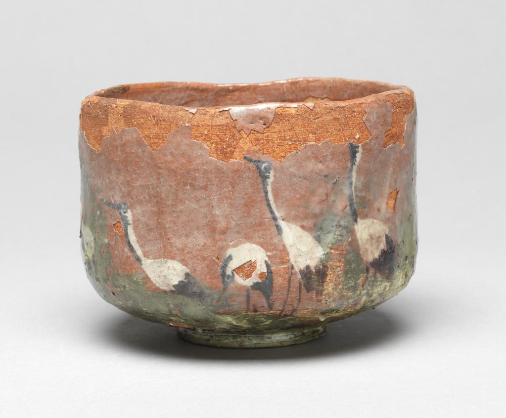 An image of Japanese pottery. Tea Bowl. Unknown pottery, Japan, Kyoto. Footed cylindrical tea bowl with bright orange-red body. Underglaze decoration of seven cranes in a green and white landscape, the whole covered with a clear glaze which has degraded. The foot and the base of the bowl appear to be covered with a clear varnish. Earthenware, hand built with clear underglaze, brush painting decoration, height 8.70 cm, diameter, rim, 11.90 cm, largest, diameter, bowl, 12.00 cm, diameter, foot, 5.50 cm, circa 1775-circa 1825. Edo period (1615-1868) / Meiji period (1868-1912).