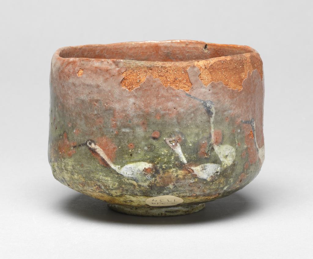 An image of Japanese pottery. Tea Bowl. Unknown pottery, Japan, Kyoto. Footed cylindrical tea bowl with bright orange-red body. Underglaze decoration of seven cranes in a green and white landscape, the whole covered with a clear glaze which has degraded. The foot and the base of the bowl appear to be covered with a clear varnish. Earthenware, hand built with clear underglaze, brush painting decoration, height 8.70 cm, diameter, rim, 11.90 cm, largest, diameter, bowl, 12.00 cm, diameter, foot, 5.50 cm, circa 1775-circa 1825. Edo period (1615-1868) / Meiji period (1868-1912).