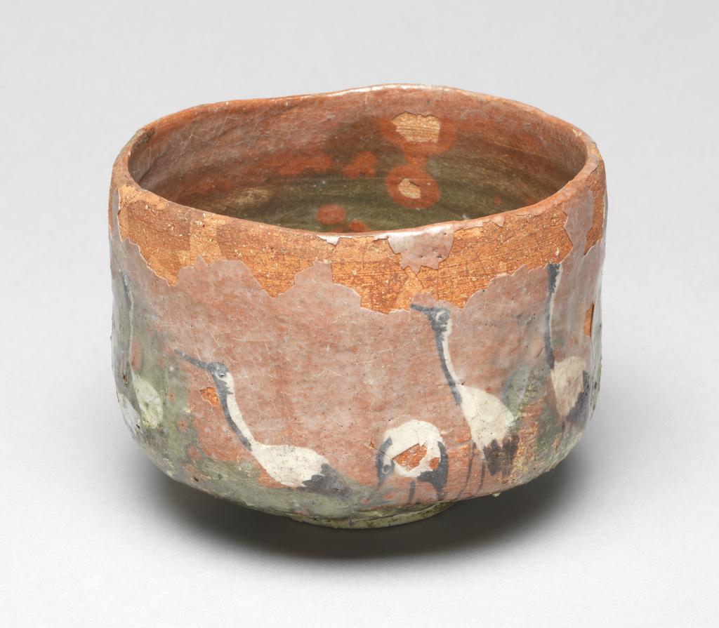 An image of Japanese pottery. Tea Bowl. Unknown pottery, Japan, Kyoto. Footed cylindrical tea bowl with bright orange-red body. Underglaze decoration of seven cranes in a green and white landscape, the whole covered with a clear glaze which has degraded. The foot and the base of the bowl appear to be covered with a clear varnish. Earthenware, hand built with clear underglaze, brush painting decoration, height 8.70 cm, diameter, rim, 11.90 cm, largest, diameter, bowl, 12.00 cm, diameter, foot, 5.50 cm, circa 1775-circa 1825. Edo period (1615-1868) / Meiji period (1868-1912).