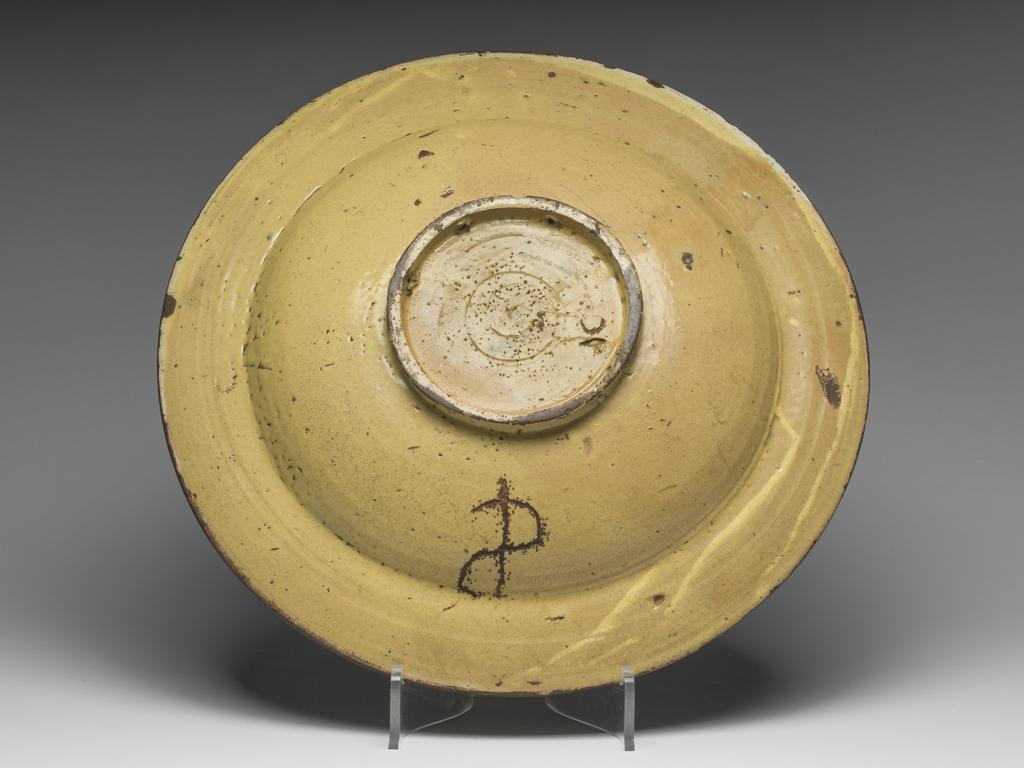 An image of Maiolica. Dish/piatto da pompa. Possibly made by a member of the Masci family of Deruta. Shape 61. Circular, with slightly sloping rim, and wide deep well, standing on a footring pierced by three incorrectly placed suspension holes. In the well, a young woman, half-length with her head in profile to right, faces a coiling scroll, inscribed 'LA VITA.EL.FINE.ELDI.LO DA.LASE RA.X.' (Life by its end, day by the evening, is praised). There are formal flowers in the background, and bound laurel round the edge of the well. On the rim, slanting serrated leaves alternate with stylized flowers. A band of yellow lustre encircles the outer edge. Earthenware, the front is tin-glazed; the reverse has thick, opaque, dark yellow lead-glaze. Height, whole, 7.5 cm, diameter, rim, 39.5 cm, circa 1500-1530. Renaissance.