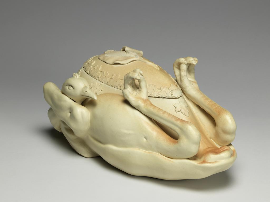 An image of Tureen and cover. ‘Pastry turkey’ tureen. John and William Turner, pottery, Staffordshire, Longton, Lane End. Moulded in the shape of a trussed and roasted fowl or game bird, breast upwards, with upturned feet and head tucked under one wing and egg-shaped cover fitting into breast. There is a relief moulded parsley garnish around the junction of the cover and body, and three moulded bay leaves which form a handle for the cover. Faint reddish-brown staining suggests roasting on parts of the upper surface. The interior is glazed. The underside is very slightly concave, with a narrow foot-rim. Cream stoneware, moulded, modelled and decorated with applied reliefs, height, whole, 15.5 cm, approx, length, whole, 33.6 cm, width, whole, 20.0 cm, approx, circa 1800. Production Note: Not dated, but social circumstances at this time indicate c.1800 the most likely date. Other examples dated c.1780-c.1820.