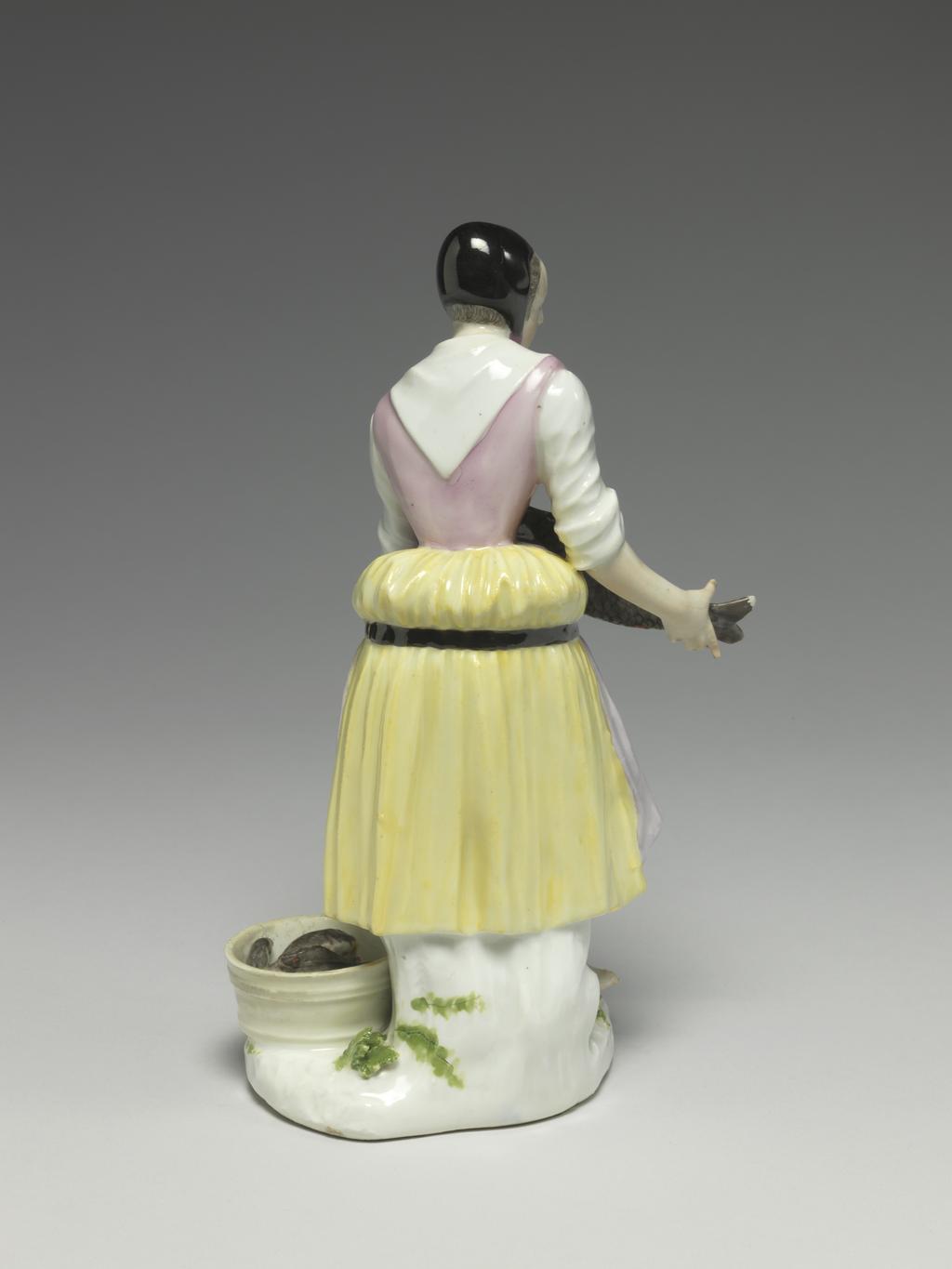 An image of Girl selling carp. Meissen Porcelain Manufactory, Saxony. Hard-paste porcelain, press-moulded, and painted in enamels. The flat underside is unglazed and has a circular ventilation hole near the back. Height, whole, 18.6 cm, width, whole, 11.2 cm, circa 1740-1745. Production Note: The figure was modelled by J.J. Kaendler after 'Carpe Vive' the 6th print in the second series of engravings entitled 'Études prises dans le bas Peuple ou les Cris de Paris' engraved by the comte de Caylus (1692-1765) after drawings by Edmé Bouchardon (1689-1762), which were published in 1737.