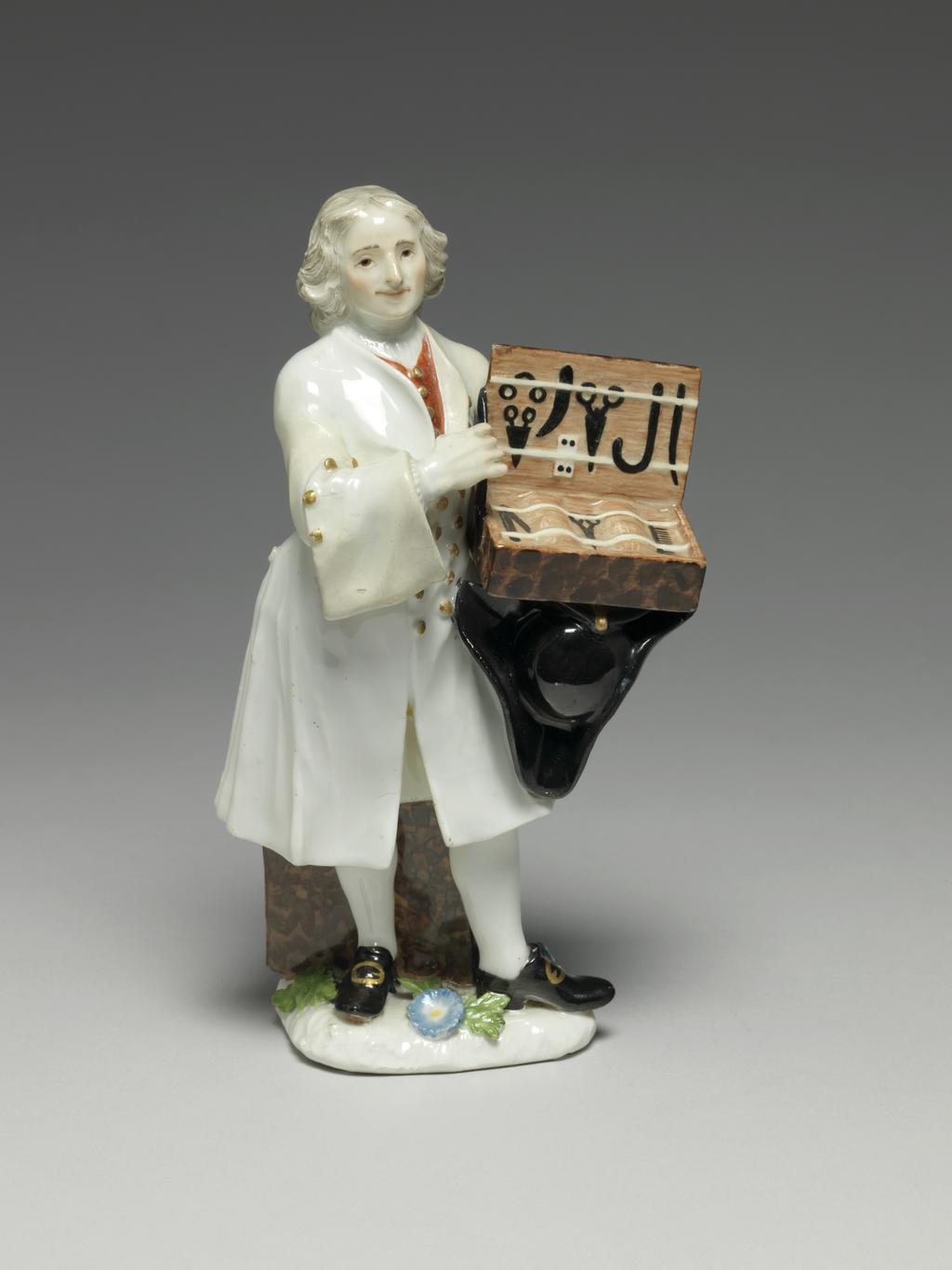 An image of A knife seller. Meissen Porcelain Manufactory. Kaendler, Johann Joachim, modeller, derived from (German, 1706-1775). Reinicke, Peter, modeller, derived from (German, 1715-1768). Hard-paste porcelain, press-moulded, and painted overglaze in enamels, and gilt. The flat underside is unglazed and has a small circular ventilation hole near the back. Height, whole, 18.7 cm, width, whole, 10 cm, depth, whole, 9 cm, circa 1745-1750. Production Note: This figure is Meissen model no. 965 which was modelled after 'Des Couteaux, des Cizeaux, des Peignes', the third print of the fourth set of prints entitled 'Études prises dans le bas Peuple ou les Cris de Paris' engraved by the comte de Caylus (1692-1765) after drawings by Edmé Bouchardon (1689-1762), and published in 1742. The figure's stance is transposed from the engraving.