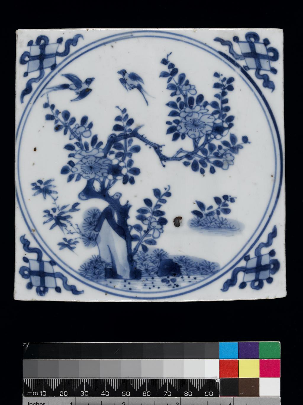 An image of Description: Tile. Hard-paste porcelain painted underglaze in blue. Square. Within a double circle is, a prunus tree, pine and bamboo (the Three Friends), a rock and two swallows; in each corner there is a lozenge, one of the Eight Precious Things. Production Notes: Chinese, K'ang HsiDimensions: height: (whole): 13.2 cm, width: (whole): 13.2 cmPeriod : 17th Century - early 18th Century, Kangxi Period (1662-1722)   