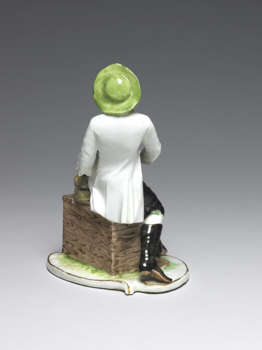 An image of Cheesemonger. Nymphenburg Porcelain Factory, Bavaria. Bustelli, Franz Anton, modeller (Swiss, 1723-1763). Hard-paste porcelain, press-moulded, glazed, and painted in enamels and gilt; the closed underside is unglazed and has a circular ventilation hold in the middle. Height, whole, 17 cm, width, base, 12 cm, circa 1755-1765. Rococo. Production Note: This is one of several street traders modelled by Bustelli in 1755 and may have been made at Neudeck between 1755-60 or after the factory moved to Nymphenburg in 1761.