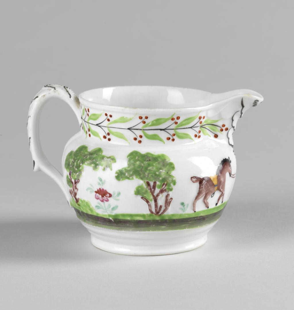 An image of Jug.  New Hall Porcelain Factory, Staffordshire, New Hall. With a hunting scene and a leaf and berry border painted in polychrome enamels. The bulbous jug stands on a low foot, and has a short cylindrical neck with a projecting lip. The strap handle is moulded with leaves in relief, and has a projecting finger rest near the lower end. On the sides, two men on horseback are galloping to the left towards a deer attacked by hounds beside a tree, and another man on foot who is brandishing a whip in one hand and holds the reigns of his horse in the other. On the other side is his horse trotting to the right, and behind it, two trees with a stylized flowering plant between them. Round the neck there is a continuous black stem bearing paired green leaves and paired black stalks with three red berries on each. The leaves on the back of the handle are outlined in black and have black dotted central vein. Bone china, moulded with decoration in relief, painted overglaze in blue, green, yellow, red, brown and black enamels, height, whole, 8.5 cm, length, whole, 12.5 cm, circa 1818-1825.