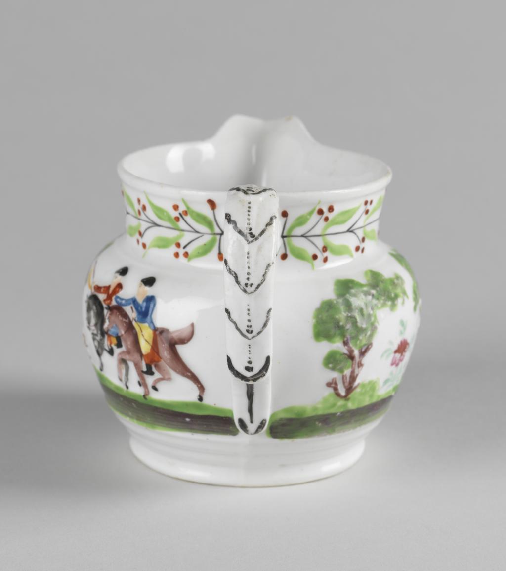 An image of Jug.  New Hall Porcelain Factory, Staffordshire, New Hall. With a hunting scene and a leaf and berry border painted in polychrome enamels. The bulbous jug stands on a low foot, and has a short cylindrical neck with a projecting lip. The strap handle is moulded with leaves in relief, and has a projecting finger rest near the lower end. On the sides, two men on horseback are galloping to the left towards a deer attacked by hounds beside a tree, and another man on foot who is brandishing a whip in one hand and holds the reigns of his horse in the other. On the other side is his horse trotting to the right, and behind it, two trees with a stylized flowering plant between them. Round the neck there is a continuous black stem bearing paired green leaves and paired black stalks with three red berries on each. The leaves on the back of the handle are outlined in black and have black dotted central vein. Bone china, moulded with decoration in relief, painted overglaze in blue, green, yellow, red, brown and black enamels, height, whole, 8.5 cm, length, whole, 12.5 cm, circa 1818-1825.