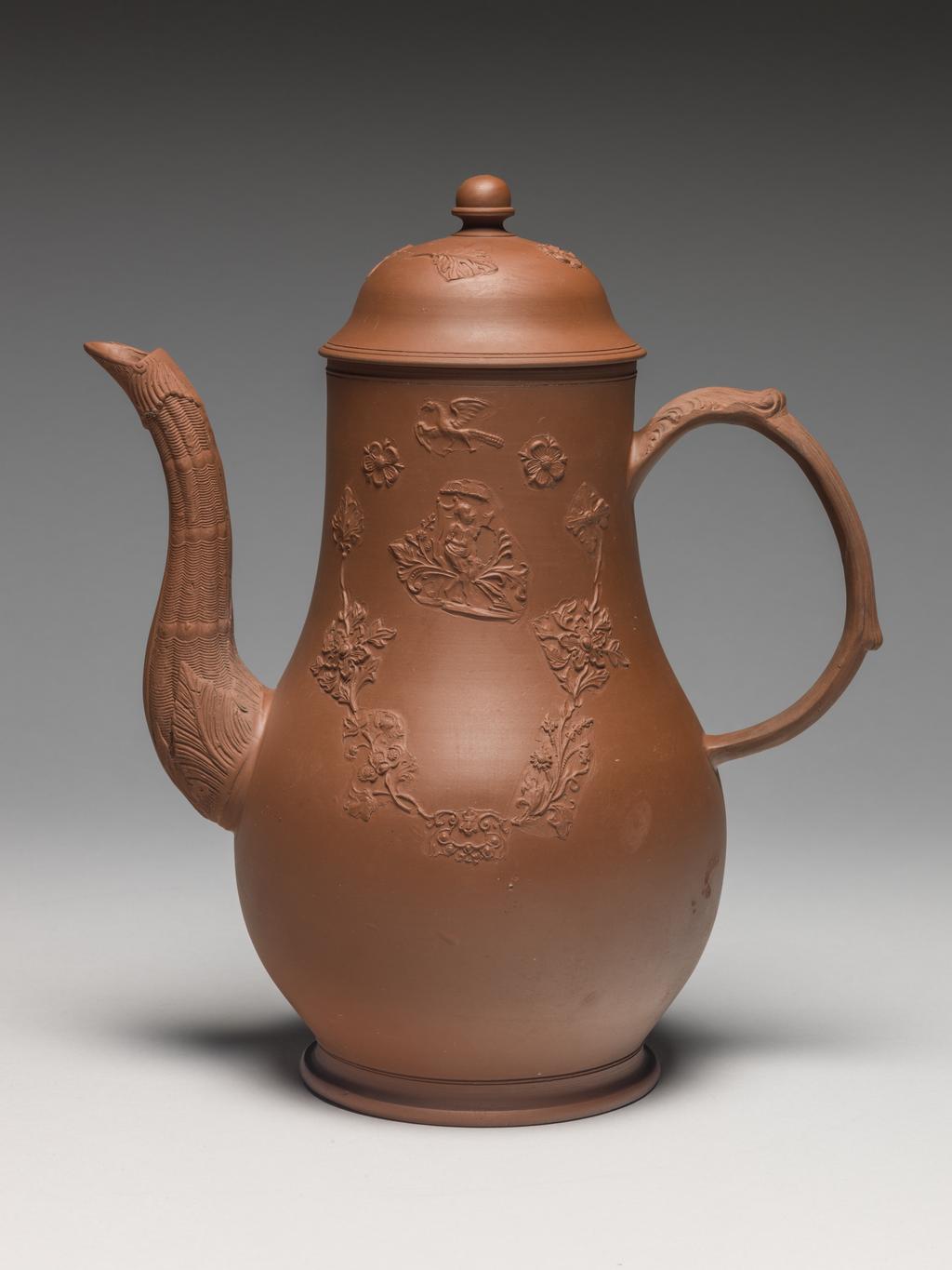 An image of Coffee pot and cover. Unknown Staffordshire factory. The body thrown, with applied moulded handle and spout, and mould applied sprigging. The pot is pear-shaped with a long curved spout moulded with wicker pattern and foliage, and a loop handle. One side is decorated with a mould-applied figure of Britannia with lion and Union Jack shield, on which is the number '45'; on the other side there is a grotesque Chinese figure seated under a parasol. Above both figures there is a flying bird, and below a festoon of mould applied stylized flowers and scrollwork. The domed cover is decorated with a similar bird and flowers, and has an acorn-shaped knob. Red dry-bodied stoneware, circa 1763-1765. Rococo.