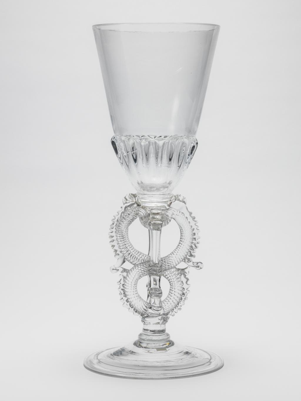 An image of Ceremonial goblet/drinking glasses. Unknown glassmaker. Heavy, moulded gadrooning on base of bowl and on cover; figure-of-eight stem; folded foot; cover finial composed of trailed and dentilated scrolls to either side of a tall spire constructed of a series of knops. Clear lead-glass, bowl blown, height, goblet, 37.5 cm, diameter, goblet, 15.5 cm, height, cover, 14.4 cm, diameter, cover, 15.4 cm, circa 1713.
