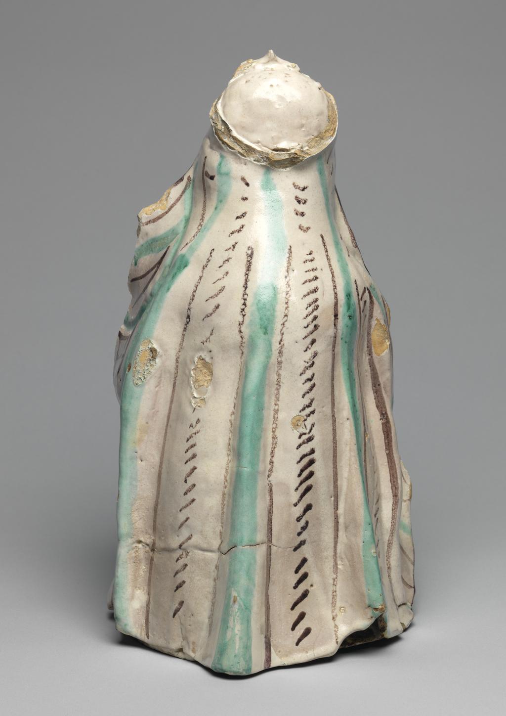 An image of Maiolica arcaica figure group. Standing Virgin and Child. Unidentified Orvieto pottery, Umbria. The Virgin stands holding the infant Christ in her left arm. Christ wears a skirt, and she wears a long pleated gown and a cloak over her head which falls down over her shoulders to the ground. The Virgin's costume is decorated with vertical rows of slanting manganese and green strokes between wide green and narrow manganese stripes. Christ's skirt has close-set stripes of alternate colours. The figure of the Virgin is hollow and the head was made separately and set into the body before firing. Greyish-buff earthenware, tin-glazed greyish-white on the exterior, and painted in manganese and copper-green, height, whole, 32.0 cm, depth, front-back, 18.0 cm, circa 1350-1450.