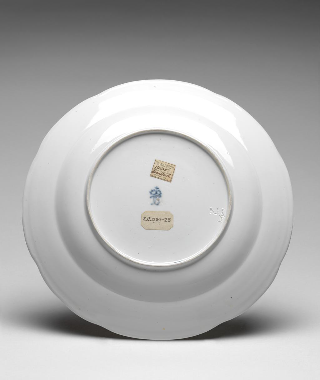 An image of Trial plate. Frankenthal Porcelain Factory, Germany, The Palatinate. Circular with eight slight arcs on the edge, sloping concave rim, shallow curved sides, and flat centre, standing on a footring. Decorated in the centre with a gold crown of TC monogram (Carl Theodore) surrounded by a sunburst with wavy rays. Around this are thirty radiating compartmens outlined in gold, each painted with a spray of flowers. On the sides of the well is an inscription in Latin VARIANTIBVS FLOSCVLIS DIVERSIL COLORES FABRICA SVB REVIVI GENTIS SOLIS HVIVS RADIIS EXVLTANTIS IN FRANKENTAAL. Hard-paste porcelain, moulded, painted in enamels, and gilded, height 3.2 cm, diameter 24.7 cm, circa 1775. Rococo. Notes: Carl Theodore was the Elector Palatine.
