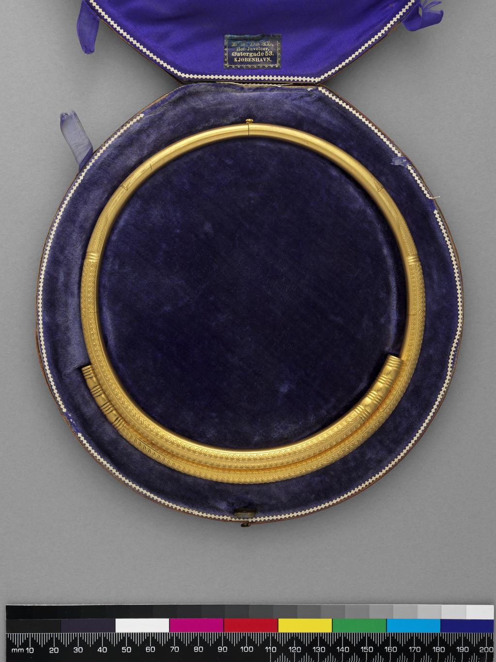 An image of Jewellery. Torc. Dahl, Emil Ferdinand (Danish, d. 1879). Formed by two overlapping tubes, each with a concealed hinge, fastening at centre back. Inscribed on the underside at the front 'M. Halkett d 24 Debr 1868'. In original light red leather case (A), lined with purple velvet and silk, bearing a black label, printed in gold 'E.F. DAHL,/ Hof-Juveleer,/ Østergade 53./ KJØBENHAVN’. Gold with engraved decoration, diameter, whole, 14.6 cm, circa 1857 to circa 1868. Archaeological Style. Acquisition Credit: Given by Mrs J. Hull Grundy. Production Note: The design of this necklet was based on a necklet, probably of the early 5th century AD found in 1857 in Øland (Hjørring county), a small island west of Aalborg in Limfjorden, now in the National Museum, Copenhagen, inv. no. 16398.