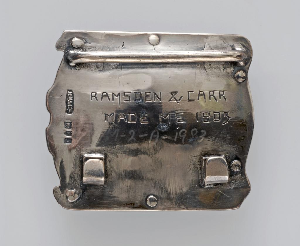 An image of Jewellery. Waist clasp. Ramsden and Carr. Ramsden, Omar (British, 1873-1939). Carr, Alwyn Charles Ellison (British, 1872-1940). Silver, chased and set with an oval plaque enamelled in blue, turquoise, green and white with a lyre bird. The silver back plate is inscribed 'RAMSDEN & CARR/MADE ME 1903'. Detached loop for the other end of the belt. Height, whole, 5.7 cm, width, whole, 5.0 cm, dated 1903. English. Acquisition: Grundy, J. Hull, Mrs.