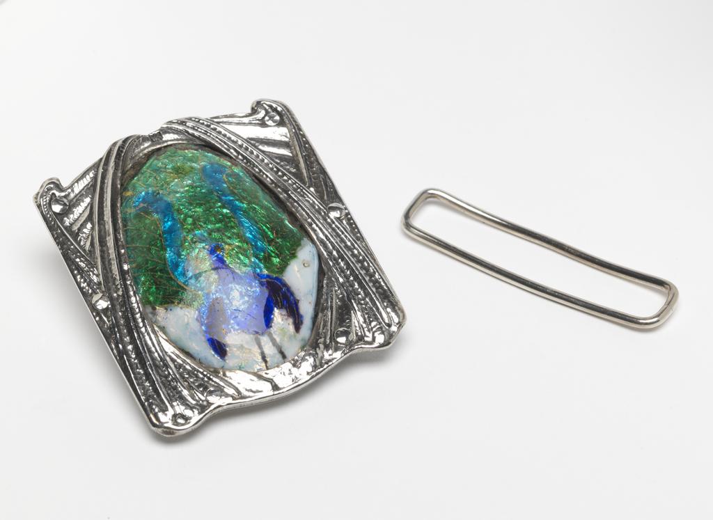An image of Jewellery. Waist clasp. Ramsden and Carr. Ramsden, Omar (British, 1873-1939). Carr, Alwyn Charles Ellison (British, 1872-1940). Silver, chased and set with an oval plaque enamelled in blue, turquoise, green and white with a lyre bird. The silver back plate is inscribed 'RAMSDEN & CARR/MADE ME 1903'. Detached loop for the other end of the belt. Height, whole, 5.7 cm, width, whole, 5.0 cm, dated 1903. English. Acquisition: Grundy, J. Hull, Mrs.