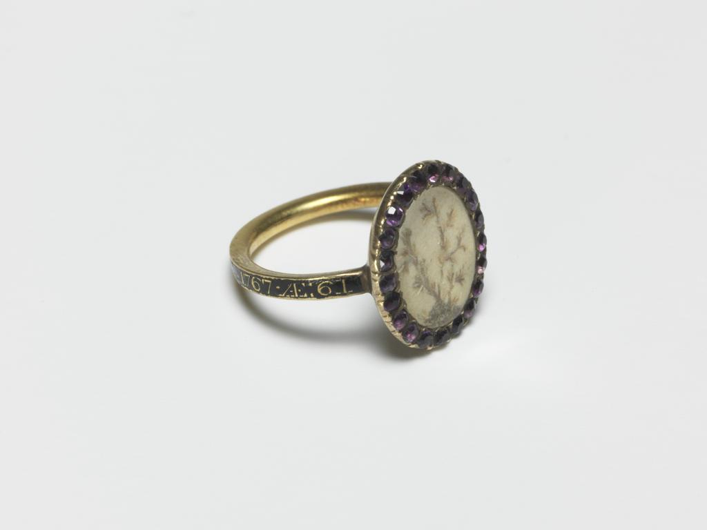 An image of Jewellery/Mourning Ring. Child's Ring. Gold, the oval bezel, with border of amethysts, containing a tree in hair on a white ground. Round the hoop, reserved on a ground of black enamel, the inscription 'FRANCES.GREENE.OB:27.JULY.1767.AE:61'. In modern red leather case (A). Diameter 1.5 cm, dated 1767. English.