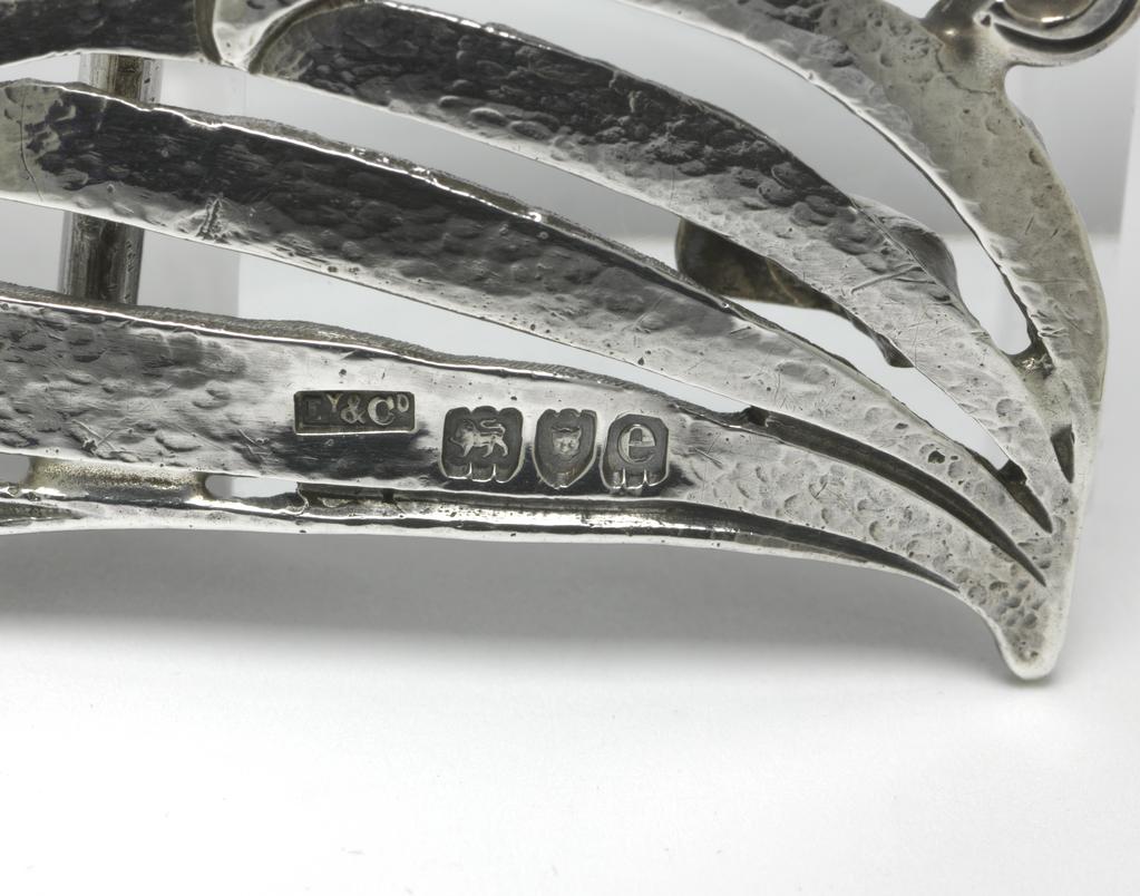 An image of Jewellery. The Planta Waist clasp. Knox, Archibald (British, 1864-1933). Cast silver openwork, in two parts, with stylised plant design. Height, whole, 5.2 cm, width, whole, 10.3 cm. Acquisition Credit: Given by Mrs J. Hull Grundy.