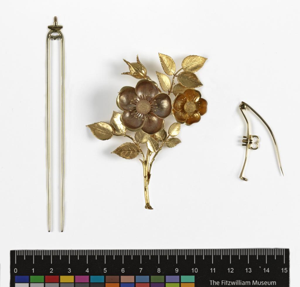 An image of Jewellery. Brooch. Hunt and Roskell, London. Gold, cast and chased in the shape of a spray of wild roses; detachable brooch-pin-fastening (A) screwed onto the back. Accompanied by a two-pronged pin (B) which converts the brooch into a hair ornament when screwed into the back in place of the pin-fastening. In rectangular maroon velvet case (C), the lid of which is lined with white silk and stamped in gold with the maker's name and address. The hair pin lies in a separate compartment in the base of the case. Height, brooch, 9.0 cm, width, brooch, 7.0 cm, length, pin, 12.1 cm, circa 1850. Acquisition Credit: Given by Mrs J. Hull Grundy.