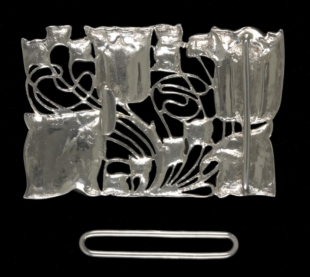 An image of Jewellery. Waist clasp. Knox, Archibald (British, 1864-1933). Rectangular with a sinuous design of two tulips and foliage. On the back, a flattened hook and a bar to hold one end of the belt. Separate rectangular loop for the other end of the belt. Cast silver openwork, height, whole, 5.1 cm, width, whole, 7.9 cm, circa 1899-1900. Acquisition Credit: Given by Mrs J. Hull Grundy.