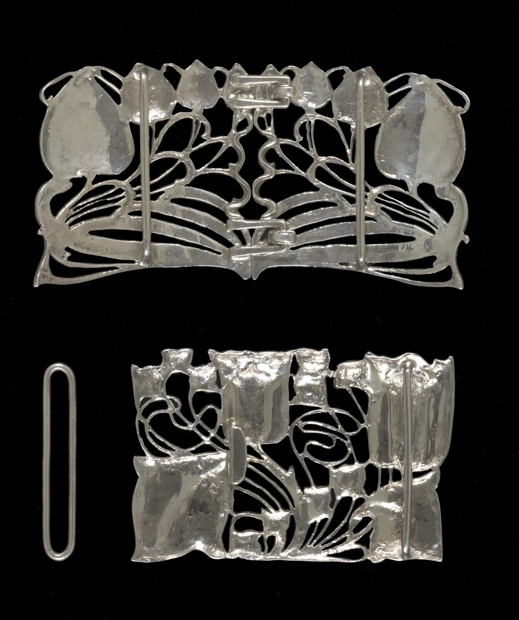 An image of Jewellery. Waist clasp. Knox, Archibald (British, 1864-1933). Rectangular with a sinuous design of two tulips and foliage. On the back, a flattened hook and a bar to hold one end of the belt. Separate rectangular loop for the other end of the belt. Cast silver openwork, height, whole, 5.1 cm, width, whole, 7.9 cm, circa 1899-1900. Acquisition Credit: Given by Mrs J. Hull Grundy.