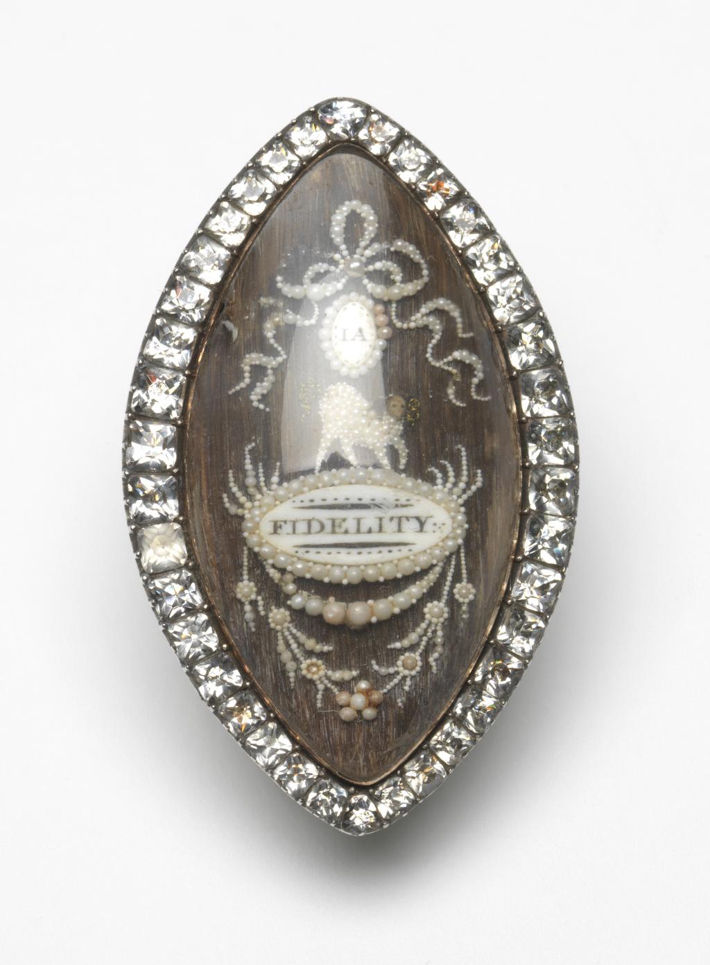 An image of Jewellery. Friendship or mourning brooch/pendant. Unknown maker, England. Of pointed oval form with a paste-set border, enclosing under a convex glass, an arrangement of ribbons, a medallion bearing the initials 'IA', a lamb or dog, a medallion inscribed 'FIDELITY' and swags on a brown hair ground; pin fastening and loop for suspension as a pendant on the back. Gold, clear pastes, seed pearls, hair and glass, height, whole, 4.5 cm, width, whole, 2.8 cm, circa 1790. Acquisition Credit: Given by Mrs J. Hull Grundy.