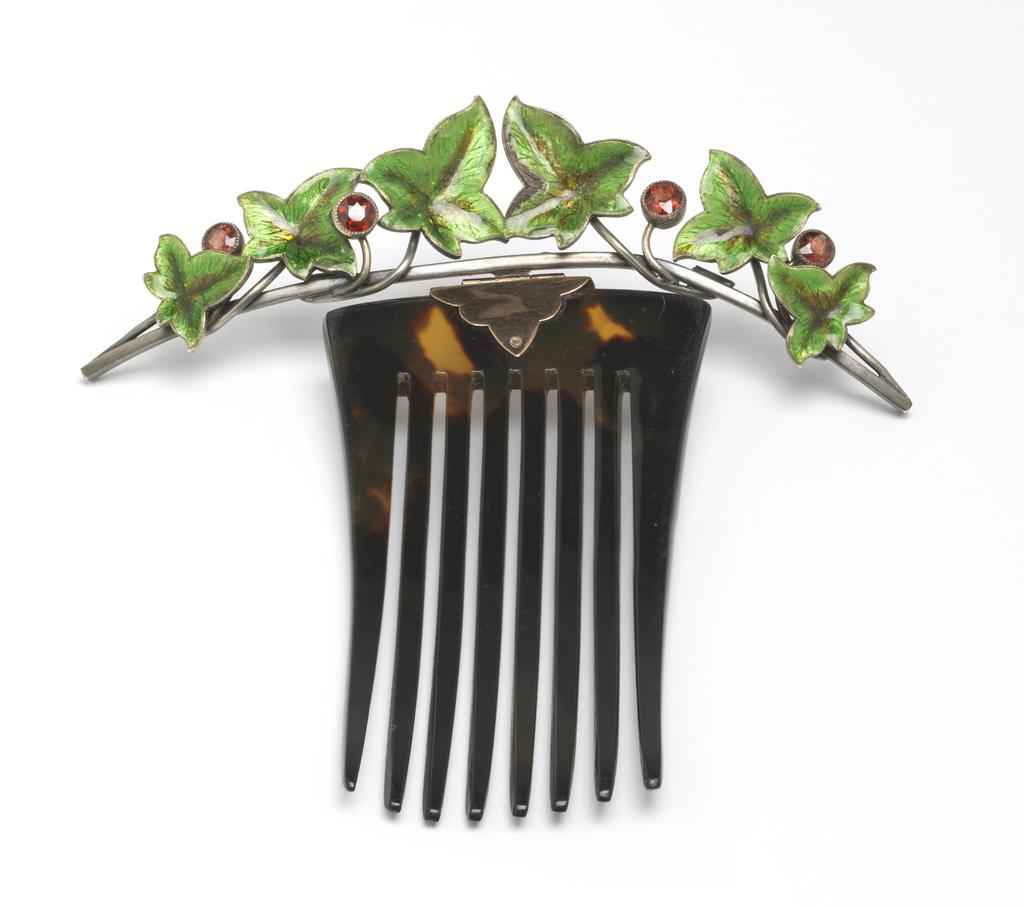 An image of Jewellery. Hair ornament. Child & Child, probably, London. Rectangular tortoise shell comb, to which is attached by means of a gold mount and hinge, a spray of silver leaves, enamelled green, and open-set garnet berries. Tortoise shell, gold, silver set with garnets and engraved and enamelled in translucent green. Height, whole, 10.5 cm, width, whole, 9.6 cm, circa 1880-1916, probably after 1891. Acquisition Credit: Given by Mrs J. Hull Grundy.