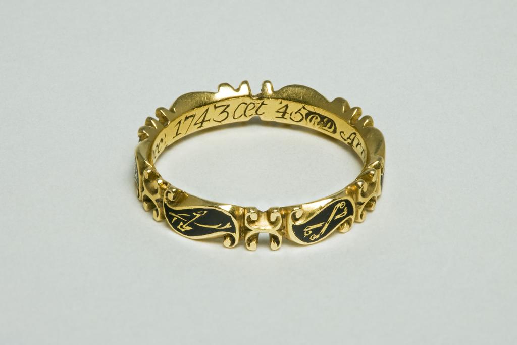 An image of Ring. Unknown Maker (English). Hoop formed of six scrolls each bearing a symbol: a skull, crossbones, a spade and mattock, an hour-glass, a coffin, and a crown of stars. Inscribed inside hoop: Arnold Rosenhagen ob Dec: 1743 æt 45. Gold, height  4.0 mm, depth 2.0 mm, length 20.5 mm, 1743.