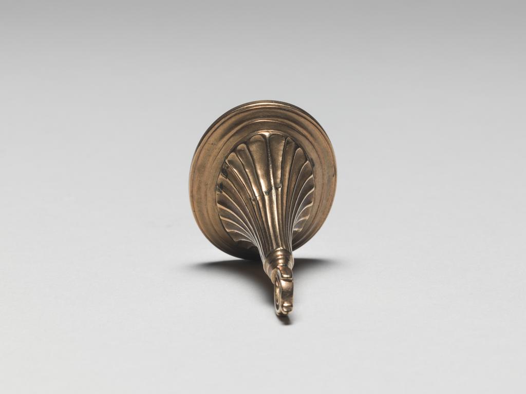 An image of Jewellery/Seal. Unknown Maker. Gold. In place of the engraved stone there is, under glass, on a ground of woven fair hair, an urn on a pedestal in white enamel and gilt metal. The pedestal is inscribed T.G. ob: 1790, round this runs the inscription in gilt metal reserved in white enamel, SACRED TO THE MEMORY OF AN ADOPTED CHILD. English. Circa 1790.