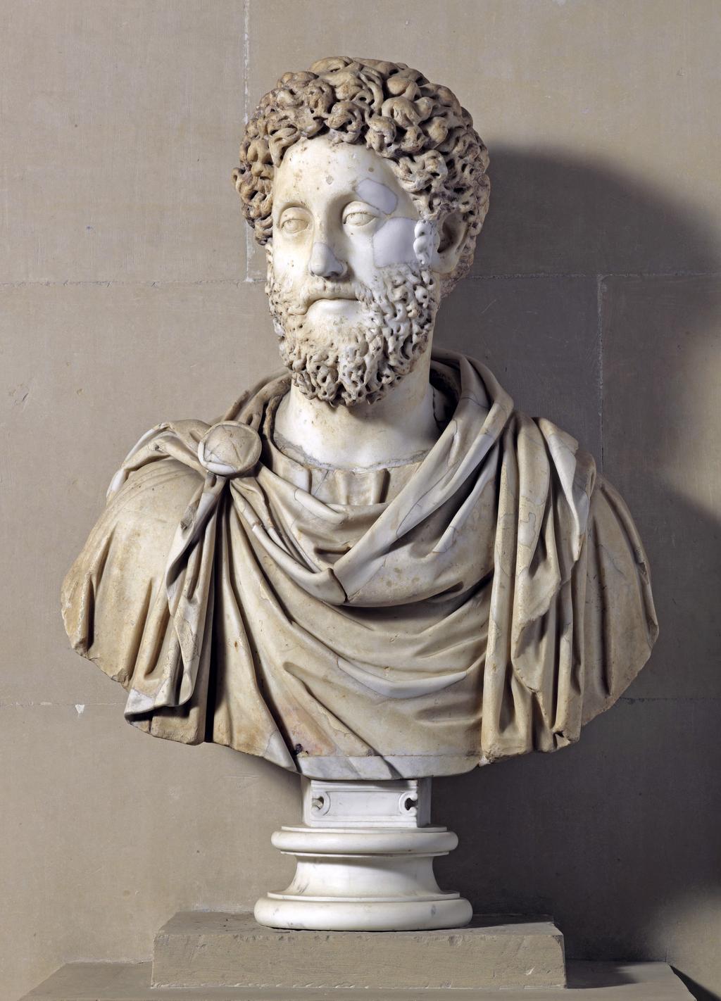 An image of Sculpture. Figure/bust. Marble bust of the Emperor Commodus (AD 180-192). Production place: Italy, Rome. A Roman marble portrait bust of the Emperor Commodus c. 191-192 AD. Over-life sized, finely sculpted, with sereneexpression gazing to the right, the heavy, hooded eyes with articulated pupils and finely carved curving brows above, his full lips above a thick, incised moustache, his luxurious beard with heavy drill work to accentuate the curls, his hair with similar drill work at the front, the back with thick undrilled curls, his ears thick with prominent earlobes, wearing a paludamentum over a tunic carved with heavy u-shaped folds below his neck, vertical folds over his left shoulder, and fastened on his right shoulder with a circular brooch, quartered within a raised border. Marble, carved and drilled, height, including socle, 32 in, height, excluding socle, 26.5 in, height, head and neck, 15 in, width, bust, 27 in, AD 180-192 AD. Notes: Accepted in lieu of inheritance tax by HM Government from the Houghton Settlement, and allocated through Arts Council England to be kept in situ at Houghton Hall.  Acquisition Credit: Accepted in lieu of Inheritance tax from Lord Cholomondeley by H.M. Governement and allocated to The Fitzwilliam Museum.