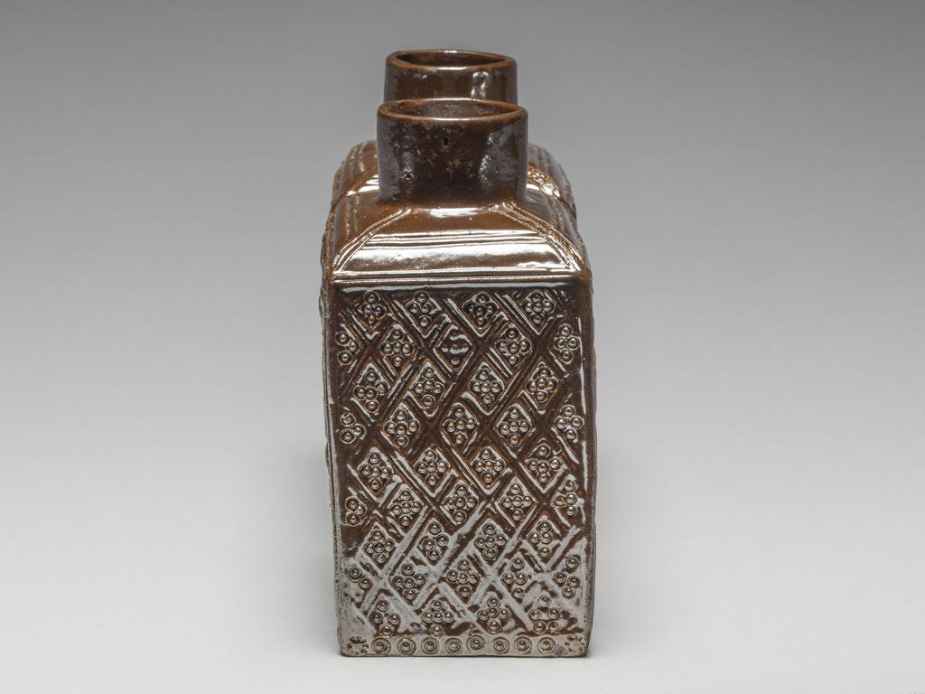 An image of Double Tea Caddy. Nottingham pottery or Crich pottery, Derbyshire. Two rectangular caddies attached by one of the narrow sides, each having a short cylindrical neck. The decoration is integrally moulded in relief on the long sides with a mermaid with a comb and mirror beside a spray of flowers, repeated four times, and on the narrow ends there is impressed trellis-diaper pattern. The initials and date 'E.H. 1770' are scratched on the base. Lustrous brown salt-glazed stoneware, moulded, height, whole, 13 cm, dated 1770. Rococo.