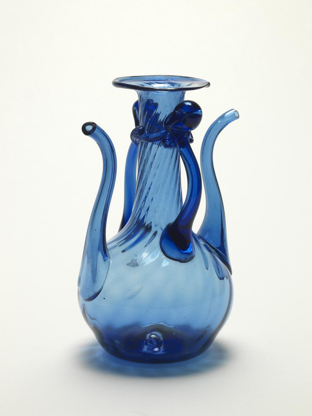 An image of Spouted Vessel. Unknown maker. Blue glass, twisted ribbed neck (reeding), two handles and two spouts, frilled collar. Height, whole, 16.8, cm, circa 1800-1900. Qajar (1779-1924). 19th-20th Century. Persian or European for the Persian market.