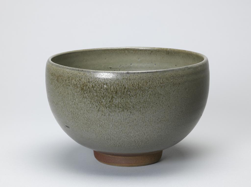 An image of Studio Ceramics. Bowl. Braden, Norah, probably (British, 1901-2001). Circular, with deep curved sides, inclining inwards slightly at the top, standing on a footring which is unglazed. Stoneware, thrown, and ash-glazed grey-green with brownish streaks and speckles, height 13.5 cm, diameter 21 cm, circa 1930-1936.