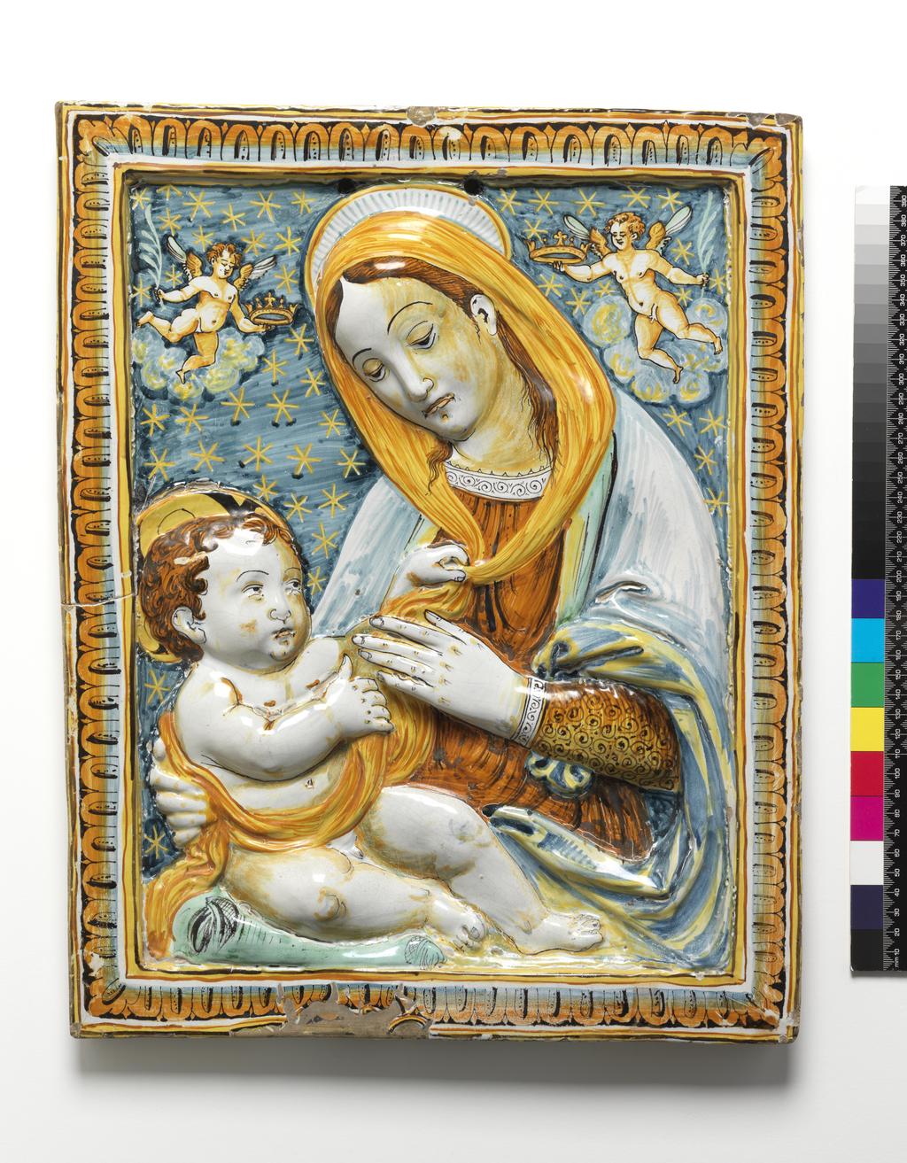 An image of Panel. Virgin and Child. Unknown maker, Umbria, Deruta. Benedetto da Maiano, sculptor, after, (Italian, 1442-1497). Maiolica panel, painted in polychrome with a half-length figure of the Virgin with the infant Christ. Rectangular, with two suspension holes inside the raised frame at top centre. Within a frame of egg and dart ornament is a half-length figure of the Virgin with the infant Christ sitting on a cushion on her lap. He plays with her veil and she restrains Him with her right hand. On each side of the Virgin's head is a cloud with a cherub flying out of it, holding a crown in the hand nearest to her and a palm in the other. The dark blue background is scattered with stars. Buff earthenware, moulded in relief and tin-glazed on the front and sides; the reverse unglazed. The glaze has crawled to the left of bottom centre. Painted in watery dark blue, pale blue, yellow, orange, and dark manganese-brown. Height, whole, 46.5 cm, width, whole, 37.0 cm, depth, whole, 3.0 cm, circa 1600-1700. Renaissance.