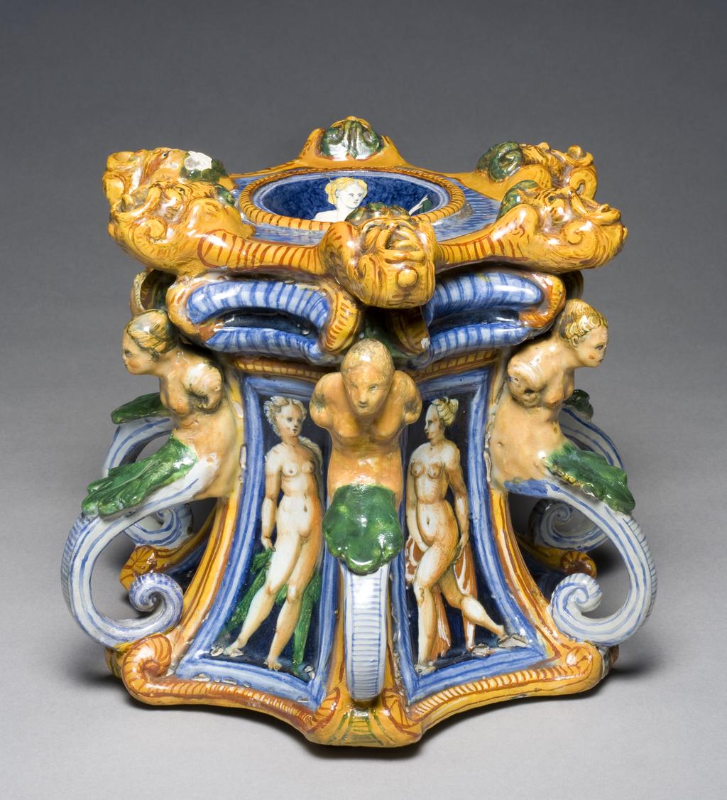 An image of Maiolica salt. Painted in polychrome with a nymph, masks, herms and female nudes. Production Place: Urbino, The Marches. Tin-glazed earthenware, height 20.0 cm, width 22.4 cm, length 27.2 cm, circa 1550-1560. Renaissance.