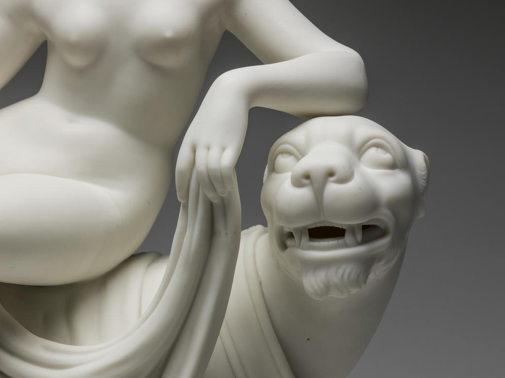 An image of Ariadne on the Panther or Voluptuousness. Minton Factory, Stoke on Trent. After the sculpture by John Heinrich von Dannecker. The figures are supported on a rectangular base with slightly sloping sides and indentations suggesting it is rocky. The panther is walking to the right with its left fore and hind legs forward, its tail between its hind feet, and its head turned towards the viewer, baring its fangs. The nude Ariadne is seated on its back with her right leg extended and her left bent.  Her head is in profile, and she rests her left fore arm on the panther's head. With her left hand she holds up a long drape which extends down to the base at the front, over the panther's back beneath her legs, and down to the back of the base. Creamy-white parian soft-paste porcelain, slip cast and assembled. Height 36.7 cm, length 30.5 cm, depth 14.3 cm, 1852. Neoclassical.