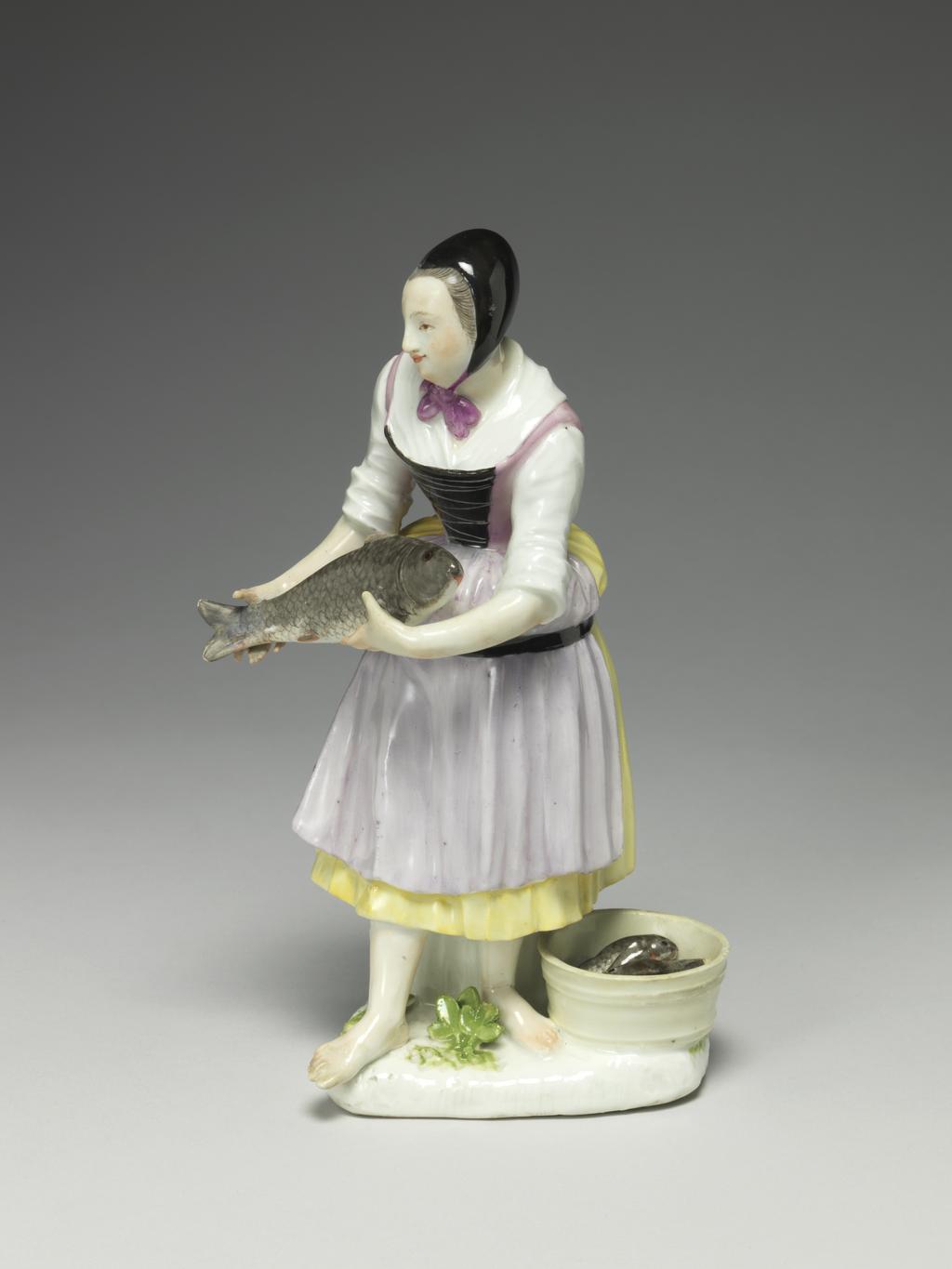 An image of Girl selling carp. Meissen Porcelain Manufactory, Saxony. Hard-paste porcelain, press-moulded, and painted in enamels. The flat underside is unglazed and has a circular ventilation hole near the back. Height, whole, 18.6 cm, width, whole, 11.2 cm, circa 1740-1745. Production Note: The figure was modelled by J.J. Kaendler after 'Carpe Vive' the 6th print in the second series of engravings entitled 'Études prises dans le bas Peuple ou les Cris de Paris' engraved by the comte de Caylus (1692-1765) after drawings by Edmé Bouchardon (1689-1762), which were published in 1737.