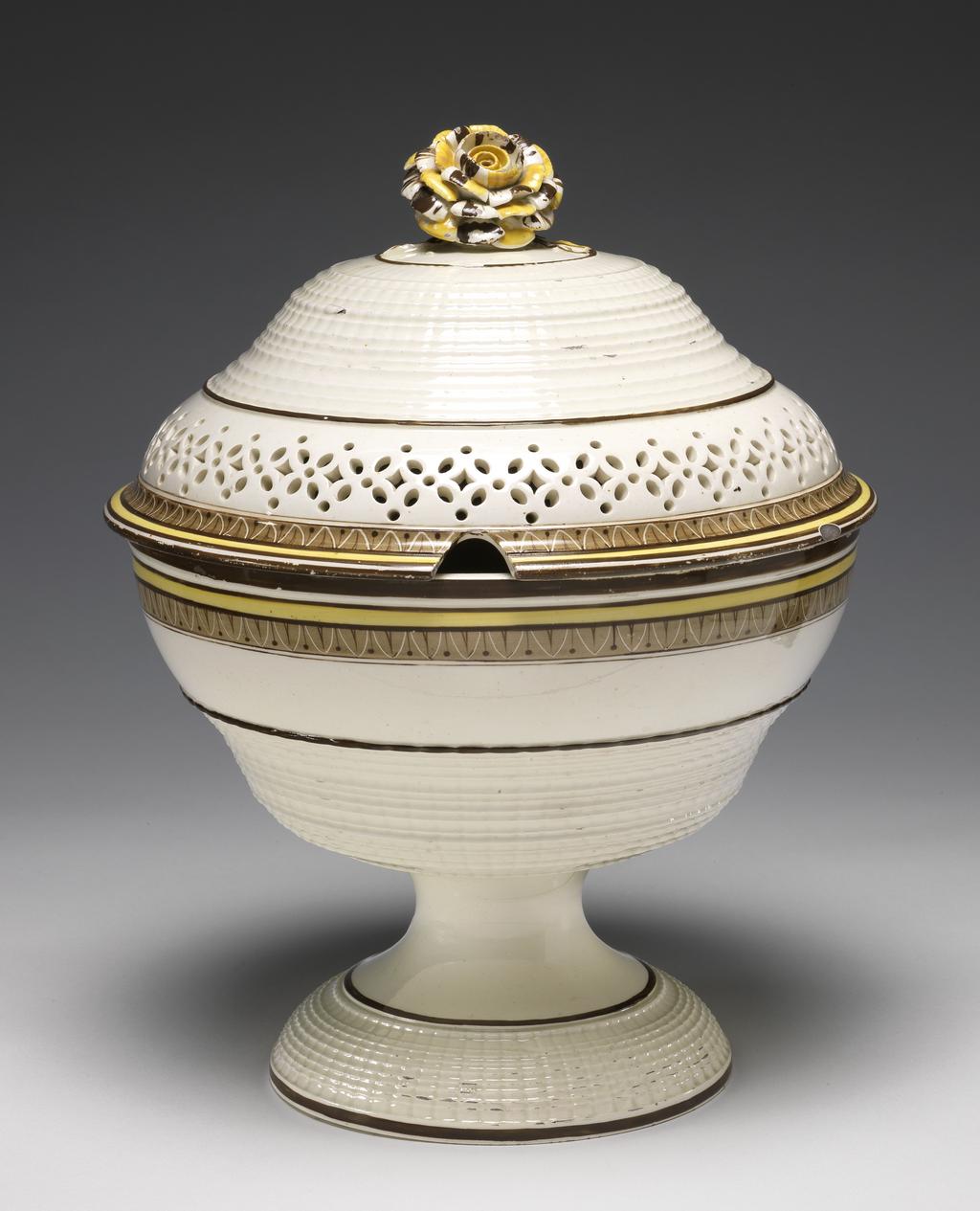 An image of Cream Bowl. James and Charles Whitehead (manufacturer, probably); Daniel & Brown (decorator, probably). The circular bowl has an ogee profile and stands on a domed spreading foot. The domed cover is also of ogee outline and has an aperture in the rim for a spoon, and a large rose-shaped knob on a stalk with three leaves and two buds. The outer edge of the foot, the lower part of the bowl and the upper part of the cover are decorated with zones of turned bands resembling basket-work, and the cover has a pierced repeating border of four-petal flowers separated by a lozenge with a circle above and below. The cover and bowl have a brown edge, borders of a yellow band between two brown, and an inner border of brown formal leaves alternating with a berry on stalk. There are horizontal brown bands on either side of the turning on the foot and cover, and above the turning on the bowl. The knob is dabbed with yellow and brown. Cream-coloured earthenware, thrown, turned, pierced, and painted in yellow and brown enamels, height, whole, 28 cm, diameter, cover, 22.3 cm, diameter, bowl, 21.2 cm, circa 1795-1810. Staffordshire, England. Neoclassical.