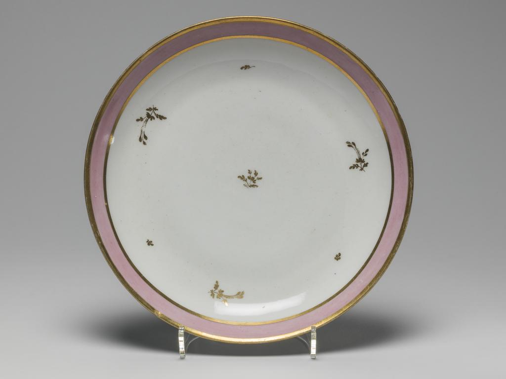 An image of Plate. New Hall Porcelain Factory, Staffordshire. Hybrid hard-paste porcelain plate, from a teaset. Decorated overglaze with a wide band of pink enamel between narrow gold bands and with scattered floral sprigs in gold. Pattern no. 223. Height 3.1 cm, diameter 20.1 cm, 1785. See C.11A-L-1988: A service comprising a teapot and cover of 'silver' shape, a milk jug, sugar basin and cover, a slop basin, two plates of different sizes, two tea bowls, two coffee cups and two saucers.