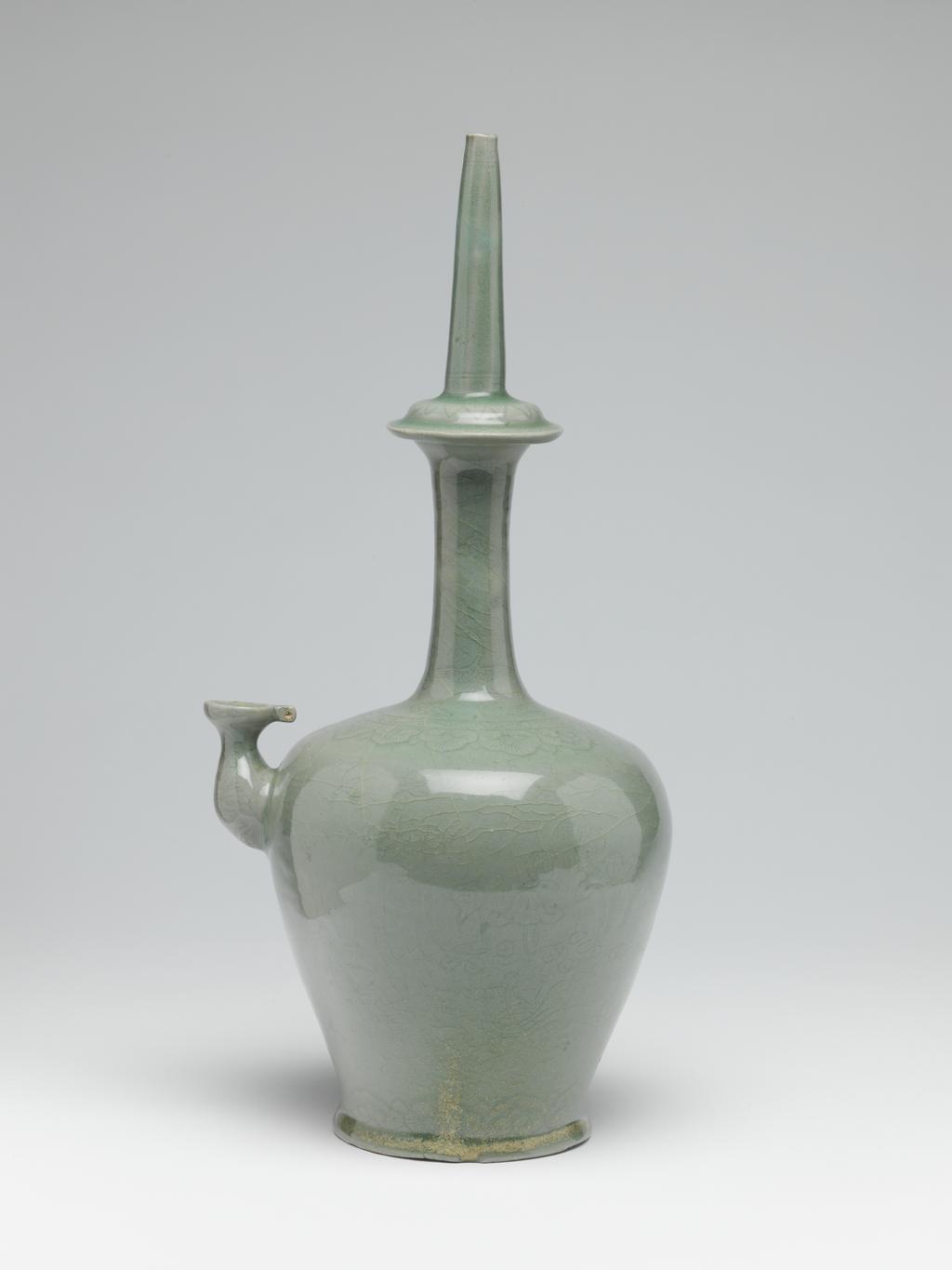 An image of Chongbyong. Kundika with willow and waterfowl design. This vessel has an ovoid body with a small spout on one side, and a long neck, with a flanged swelling in the centre. The lower part of the body contracts to a splayed footring, giving it a stable shape. The upper part of the long neck is cut into octagonal form, and has incised cloud motifs on each facet, while the projecting ring shows lotus petals and scrolling foliage. The lower part of the neck is decorated with flying cranes among clouds. A classic-scroll border and youi-heads are finely incised round the shoulder, and a key-fret border and further youi-heads round the foot. The body itself shows willow trees on one side and reeds on the other, with ducks and lotuses, flying cranes and geese delicately engraved between. Production Notes: This type of kundika, which is modelled on bronze examples decorated with silver inlay, was very popular in the Koryo dynasty. Both shape and design are very similar to the metal counterparts. The kundika (Chongbyong) was used in Buddhist ceremonies as a container for water, which was filled in through the spout and sprinkled from the narrow mouth. Similar sherds were excavated at kiln no.7, Sadang-ri, Kangjin-gun, South Cholla province, and were produced in the mature period of Koryo celadon, in the first half of the twelfth century. Production Place: Sadang-ri kilns. Kangjin-gun. South Cholla province. Korean. Stoneware, thrown, with applied lugs, incised and celadon-glazed, height (whole) 34.7 cm, diameter (maximum) 16.0 cm, diameter (foot) 9.0 cm, circa 1101 to 1150. Koryo Dynasty.