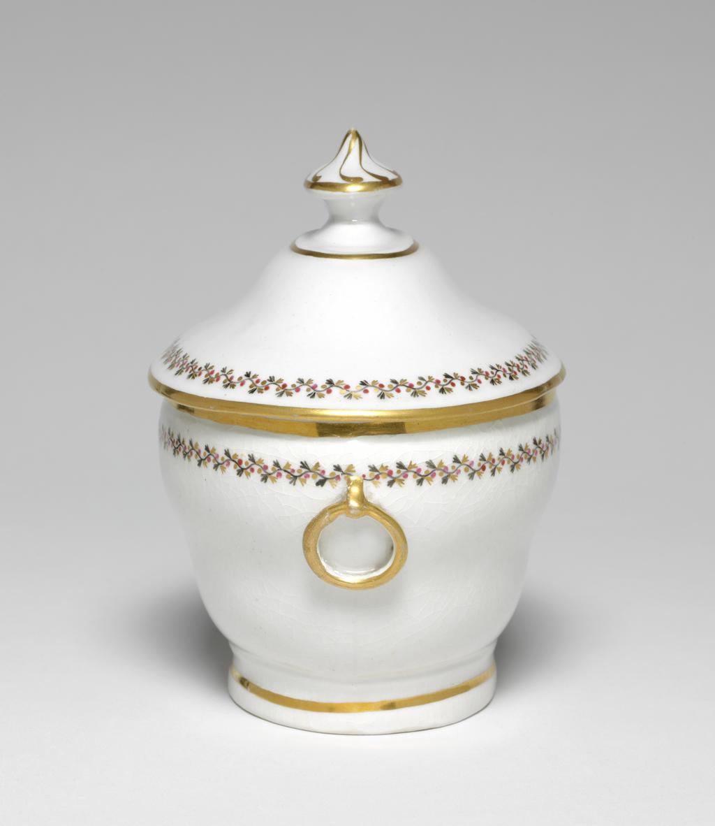 An image of Sugar Bowl/Sugar Basin. New Hall Porcelain Factory, Staffordshire. Of oval, ogee form with an applied ring handle at each end, standing on a footring. The cover is of slightly ogee form with a small oval platform and an oval pointed knob on top.The exterior of the bowl is decorated with a border comprising a black wavy stem with small trefoil leaves, puce berries, and gold trefoil leaves. The handles are gilded and there are gold bands just below the rim, and round the footring. The cover is decorated with a similar border, and with gold bands round the edge, the edge of the platform and the knob, which also has eight swirling gold lines radiating from the point. Pattern no. 280. Hybrid hard-paste porcelain, moulded, with crazed glaze, painted overglaze in black and puce enamel, and gilded. Height, whole, 14.7 cm, length, whole, 14.5 cm, width, whole, 10.5 cm, circa 1797-1803.