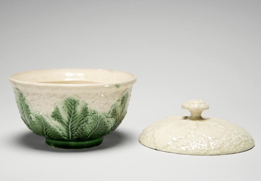 An image of Sugar bowl and cover. Cauliflower sugar basin. Wedgwood, Josiah, attributed but doubtful. Staffordshire Pottery. Of Chinese covered tea bowl form, moulded to resemble a cauliflower, the convex cover (A) with six leaves radiating from the shallow cauliflower knob. Cream earthenware, press-moulded, slip-cast and decorated with green and yellowish cream lead-glazes. The base inside the footring is only partially glazed. Height, whole, 10 cm, diameter, whole, 11.5 cm, circa 1759-1775. Rococo.