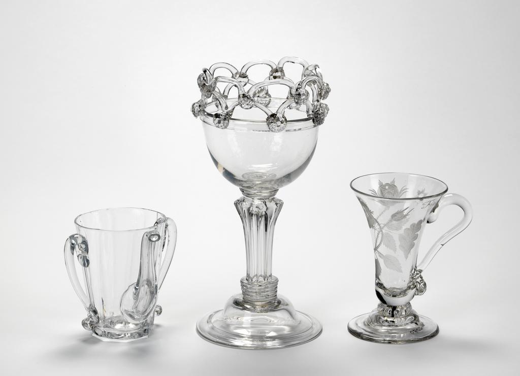 An image of C.614-1961: Sweetmeat glass/dessert glass. Unknown English glassmaker. Moulded double-ogee bowl, looped rim with prunts on triple collar and simple white opaque twist stem, domed and folded foot, moulded to match bowl. Lead-glass, bowl and foot moulded, height, whole, 16.5 cm, diameter, whole, 8.9 cm, circa 1760. Adlib numbers of others to be confirmed. One posset pot on left, engraved drinking glass on right.
