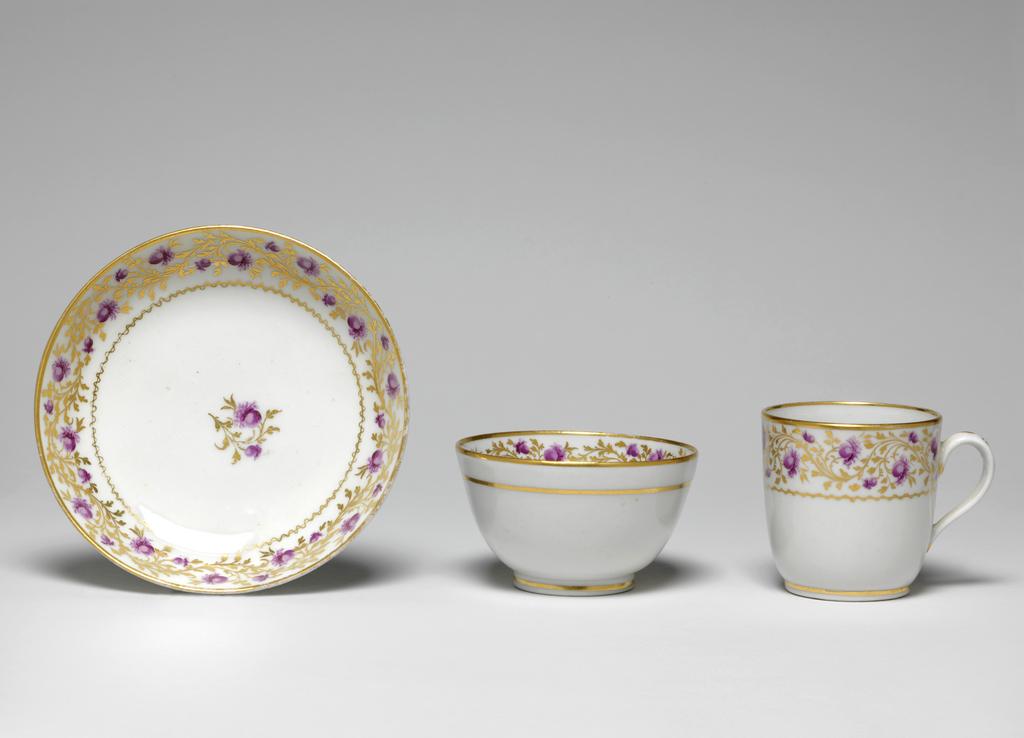 An image of Tea bowl and saucer. Coffee cup. New Hall Porcelain Factory, Staffordshire. The tea bowl has deep curved sides and stands on a footring. The saucer (A) has curved sides, a wide central area, and stands on footring. The coffee cup (B) has deep almost straight sides curving inwards slightly at the footring, and a loop handle.The tea bowl is decorated in the middle with a gold spray with two different puce flowers. Round the upper edge is a border comprising a continuous wavy gold spray of leaves with a small and a larger puce flower repeated at intervals. Below there is a wavy horizontal gold line and on the rim a plain gold band. On the exterior there is a horizontal gold band below the rim, and another round the footring. The saucer is decorated to match. The coffee cup is decorated on the outside with the same border and gold bands on the rim and footring. On the back of the handle here are three gold stylized leaf sprigs. Pattern no. 318. Hybrid hard-paste porcleain, presumed lead-glazed, painted overglaze in puce enamel, and gilded. Height, tea bowl, 5.2 cm, diameter, tea bowl, 8.8 cm, height, coffee cup, 6.5 cm, width, coffee cup, 8.6 cm, diameter, coffee cup, 6.5 cm, height, saucer, 3 cm, diameter, saucer, 13.5 cm, circa 1800-1805.