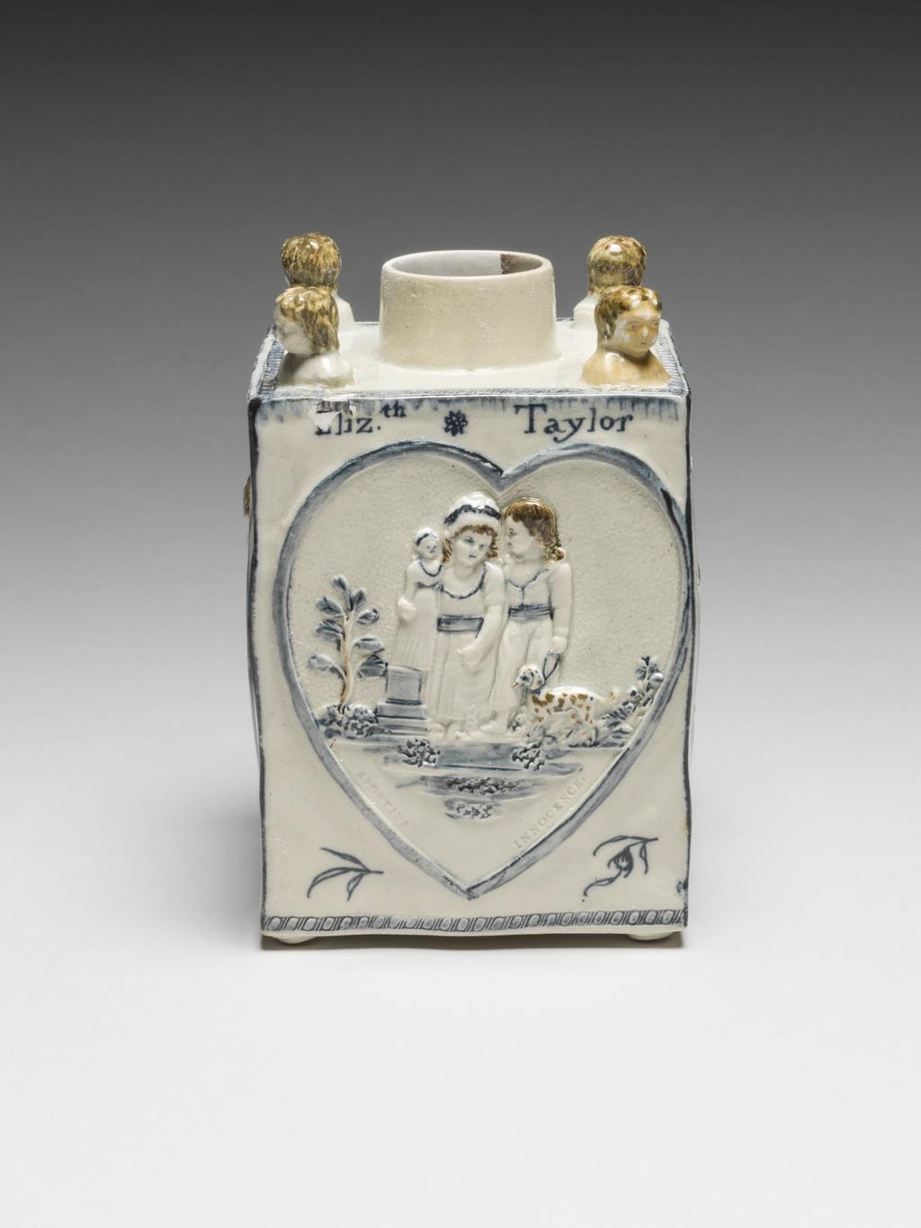 An image of Pearlware Tea Caddy. Bovey Heathfield Pottery, Devonshire. On each corner there is an applied moulded bust of a child, and on the base four coiled feet. Two opposing sides are decorated with a heart-shaped raised outline enclosing a relief of a little girl holding a doll accompanied by a little boy with a small dog on a lead, with a small tree and a low broken off colum on the left. Below them is an impressed inscription, 'SPORTIVE INNOCCENCE' .On the other two sides there is a similar heart enclosing a relief of a child holding out a bearded male mask to frighten a little girl who has fallen to the ground and raises her left hand to push it away. Below is the impressed inscription, 'MISCHIEVOUS SPORT'. In each of the lower spaces outside the heart outlines there is a painted sprig, and above one, a moth or butterfly. Painted round the top of three sides is the inscription, Eliz.th (th raised) Taylor/Born march/18th. (th raised) 1795'. Cream earthenware, moulded. Pearlware, painted underglaze in dark blue and yellowish-brown, dated 1795. English.