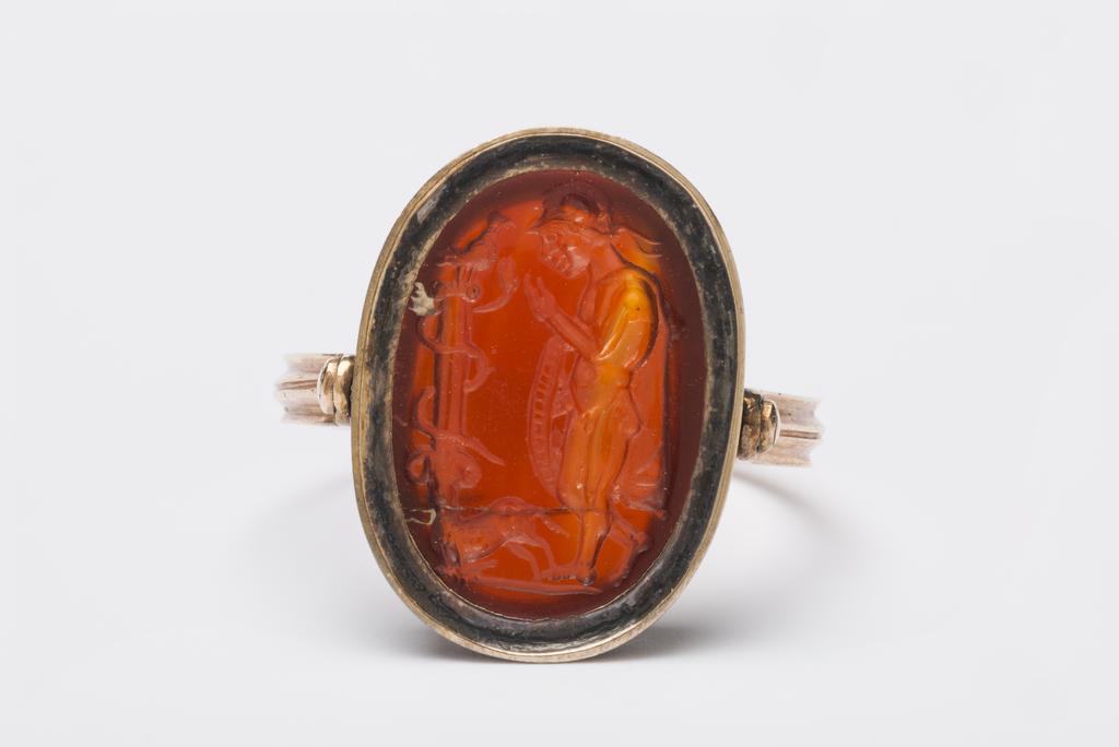 An image of Engraved Gems/Ringstone. Profile of a nude young warrior wearing only a helmet and chlamys, holding a shield. To his left stands a column entwined by a serpent on top of which sits a bird. Intaglio cutting, red-brown cornelian, height 15, mm, width 11 mm, depth 4 mm, circa 200- circa 100 B.C. Roman Republican.