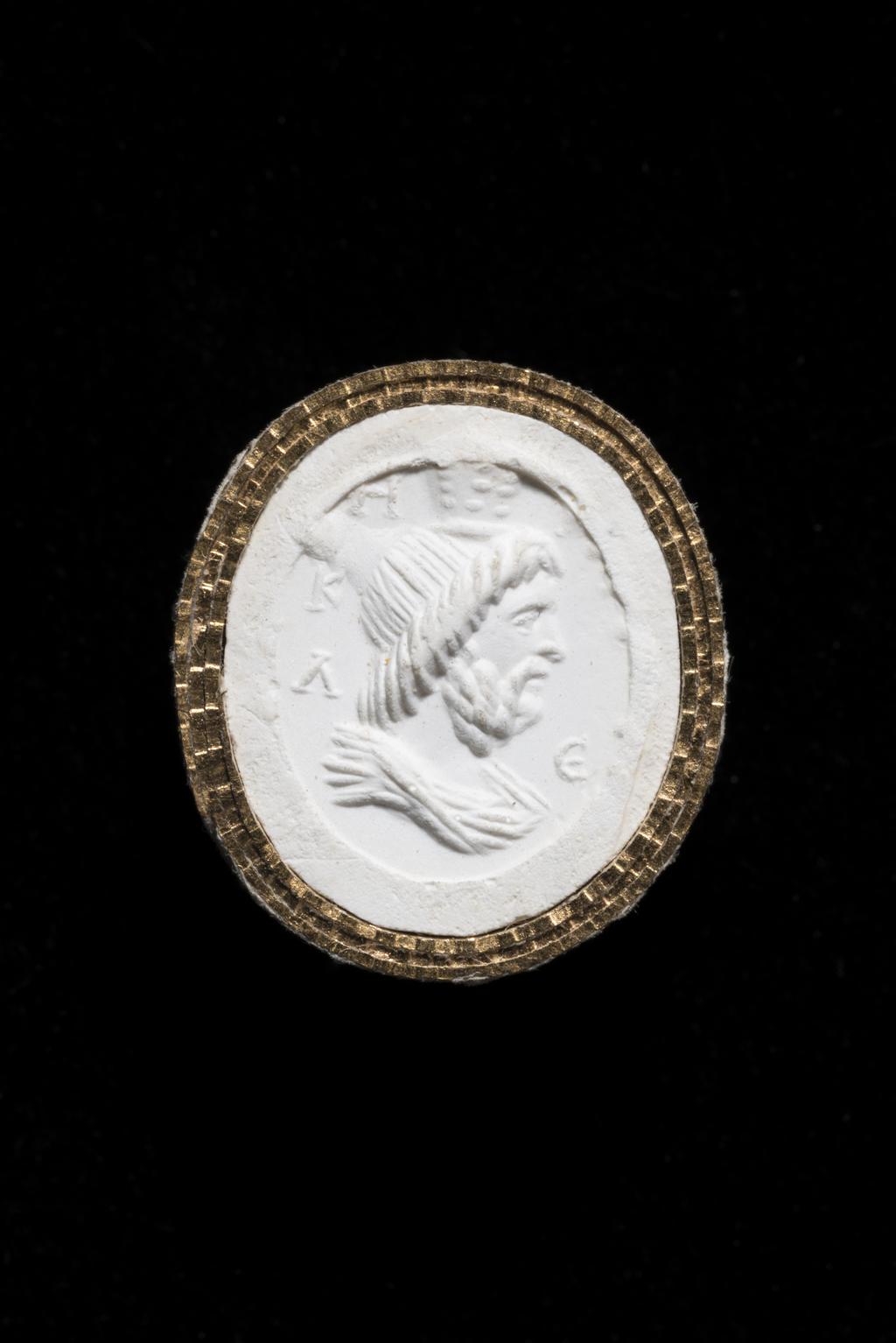 An image of Engraved gems/Ringstone. Bust of Zeus Serapis in profile to the right; shoulders draped. In the field, on the left there is a vertical inscription and on the right an E. Intaglio cutting, carnelian, 11 mm x 9 mm, circa 100-circa 200 AD. Roman Imperial.