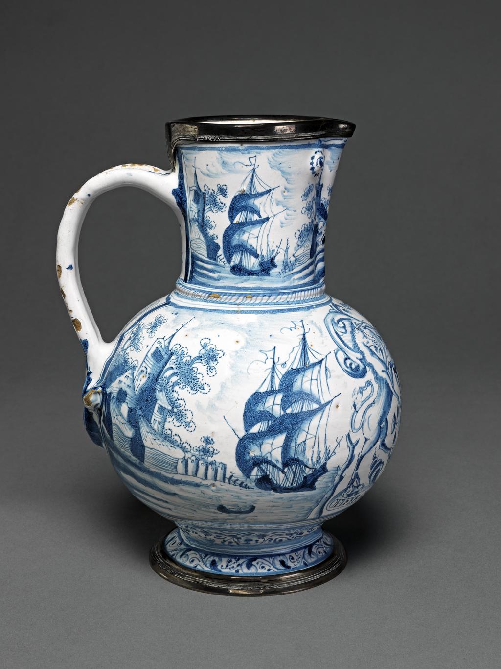 An image of Jug
English delftware
Tin-glazed earthenware painted in blue with the arms and motto of the Apothecaries' Company.
Tin-glazed earthenware painted in blue. Bulbous body with pinched up lip, and on either side of it, a small embossment to stimulate an eye; grooved loop handled divided in the form of a fleur-de-lys at the lower end; standing on a low foot. Both rim and foot mounted in silver. Decrated on the front with the full arms of the Apothecaries' Companoy with motto: 'OPIFER:QVE:PER: ORBEM:DICOR'; at the sides and on the neck, sea-shore scenes with buildings and sailing-ships. Two narrow borders of leafy scrollwork encircle the foot. Belowthe handle are the initials and date 'E.V/1650'. The mounts bear the London hallmark for 1844.
Southwark, London
England
C.1650