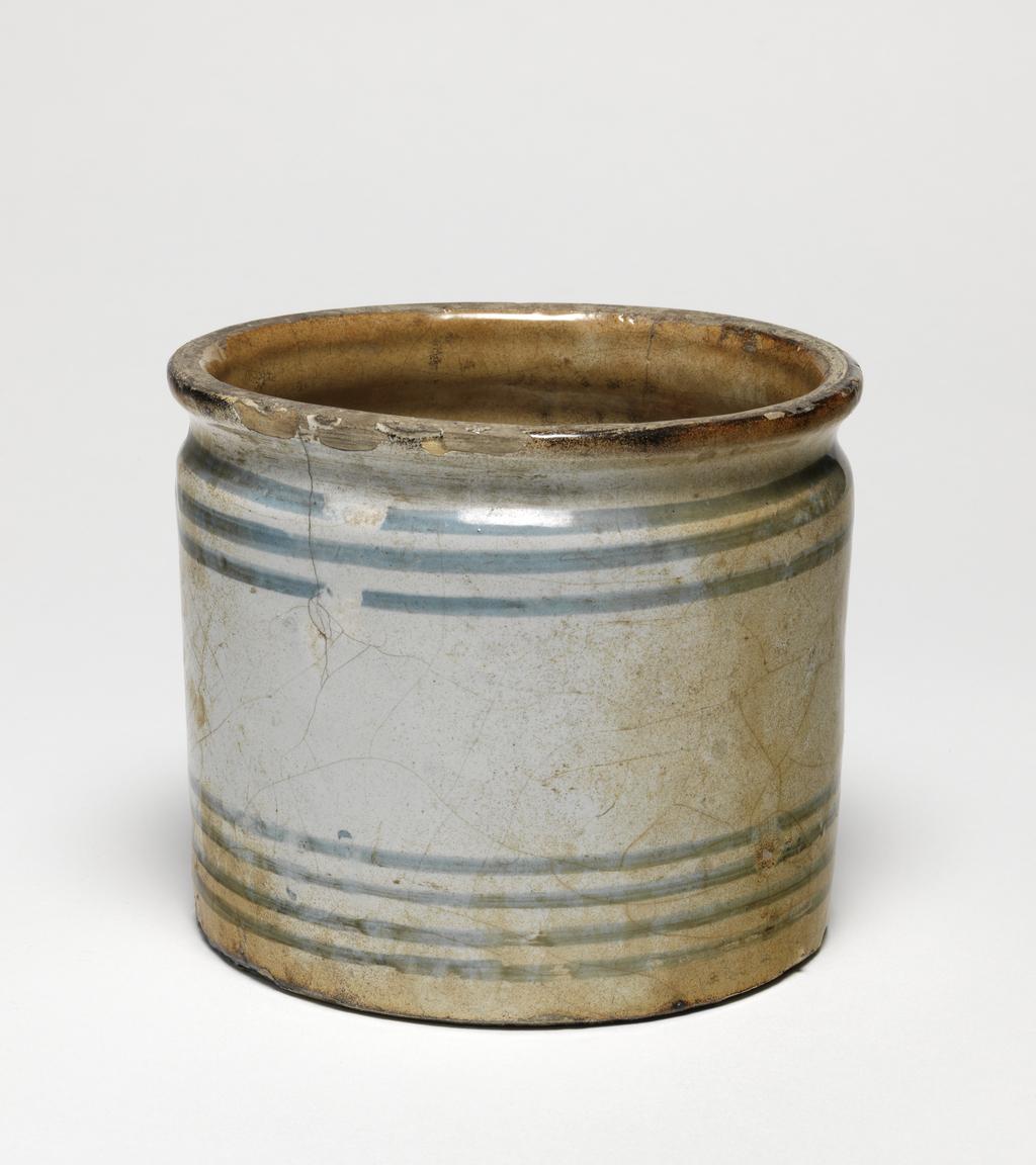 An image of English Delftware. Storage jar/dispensing pot. Unidentified London pottery, probably. The exterior is decorated with groups of horizontal stripes, three below the rim and four above the base. Buff earthenware, thrown, tin-glazed except for part of the base, and painted in blue, height, whole, 9.8 cm, diameter, whole, 11 cm, circa 1780-circa 1820. As the jar was excavated in London it seems likely to have been made there.